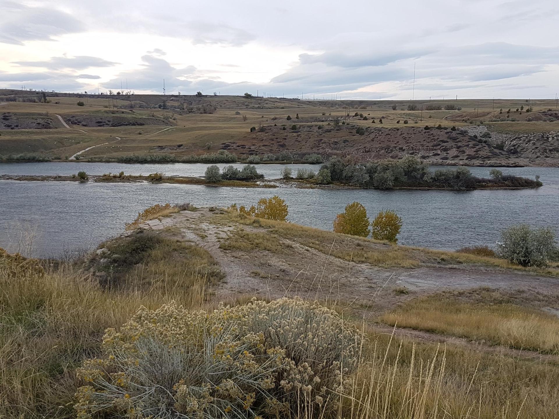 Overcast view of a river with small islands and dry, sparse vegetation.