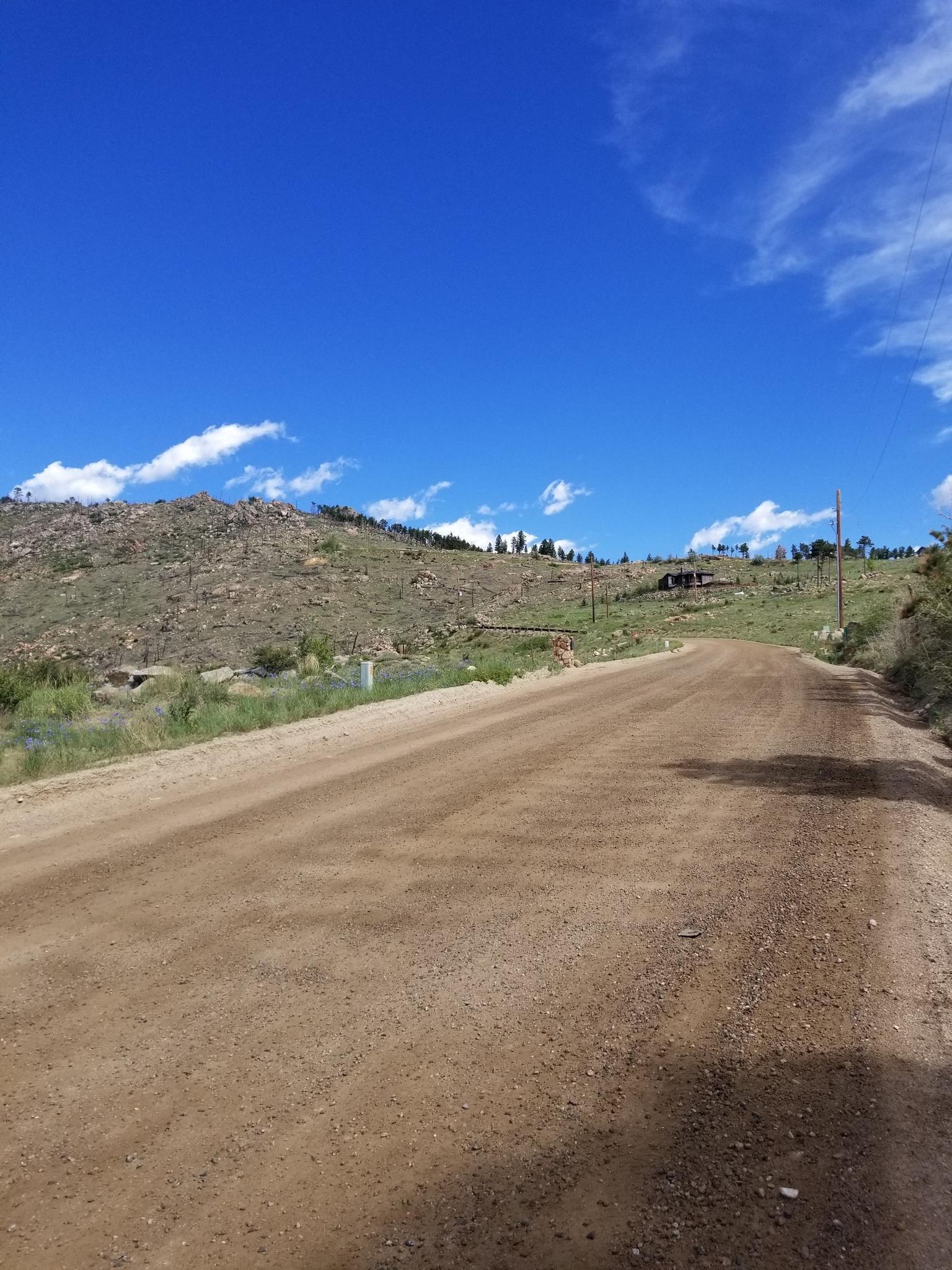A dirt road winds uphill past barren hills under a bright blue sky.