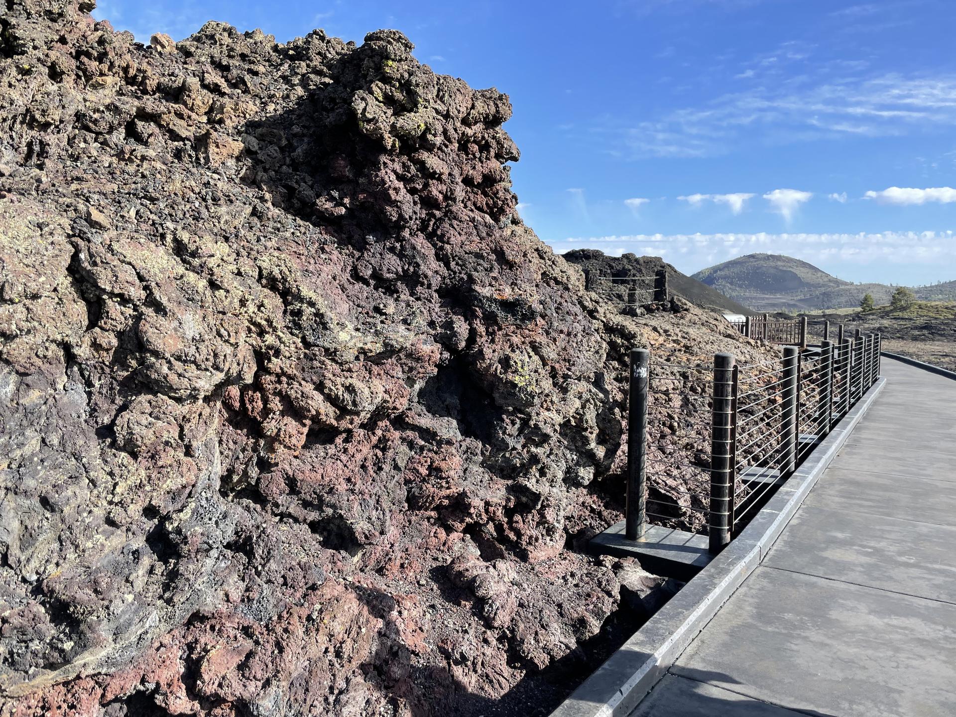 Rugged dark volcanic rock beside a paved path with a protective railing.