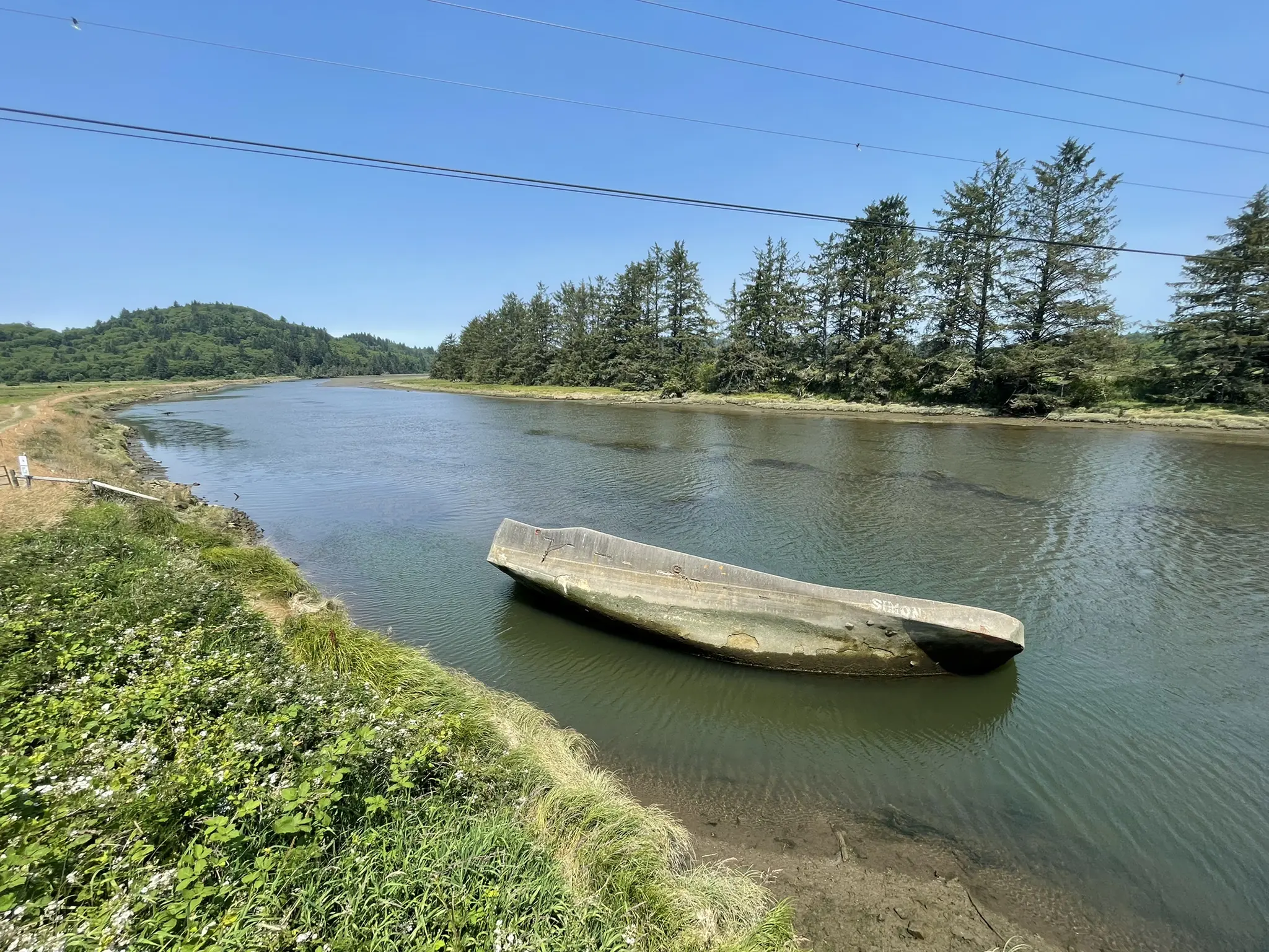 Overturned boat partially submerged in a calm river with green banks and trees.