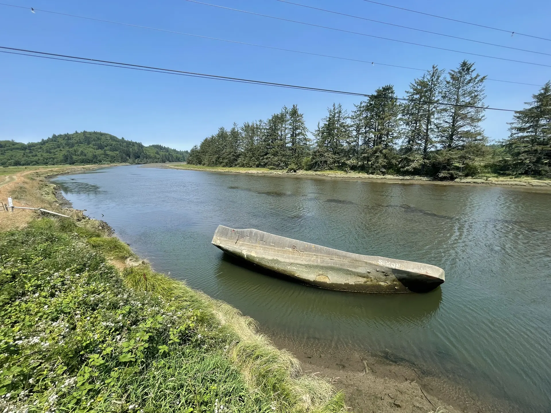 Overturned boat partially submerged in a calm river with green banks and trees.
