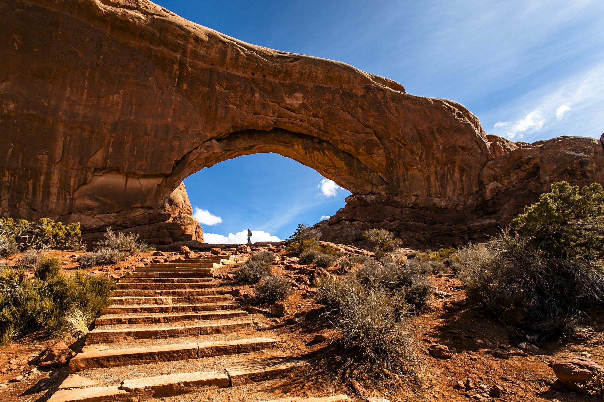 Wooden steps leading up to a large natural rock arch, person visible.