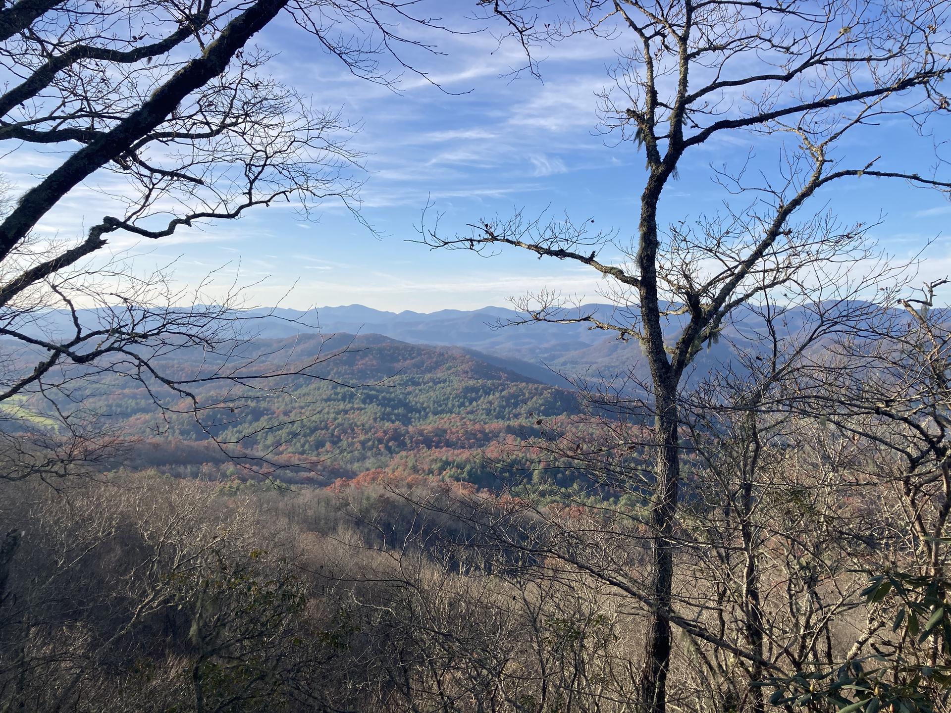 Panoramic view of rolling forested mountains under a partly cloudy blue sky.