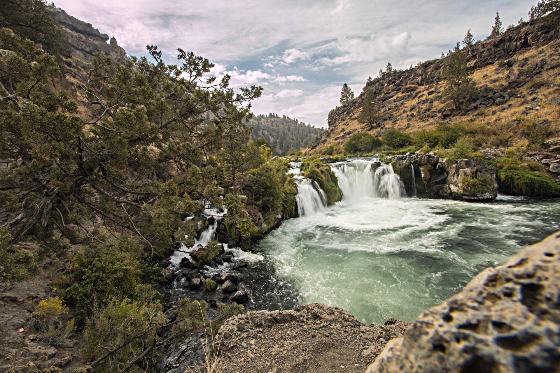 A powerful waterfall cascades into a green river within a rocky canyon.