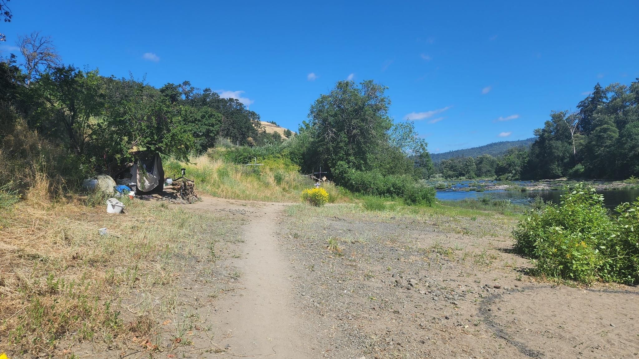 Dirt path leading to a river, with hills and trees under a clear sky. - South Umpqua Riverfront Trail