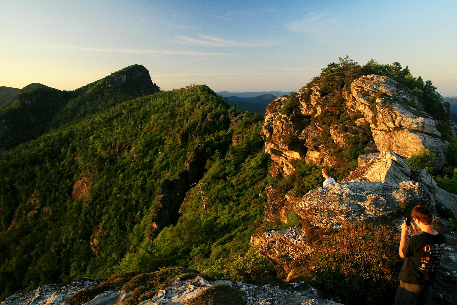 Two people on a rocky peak, enjoying a mountain sunset with golden light.