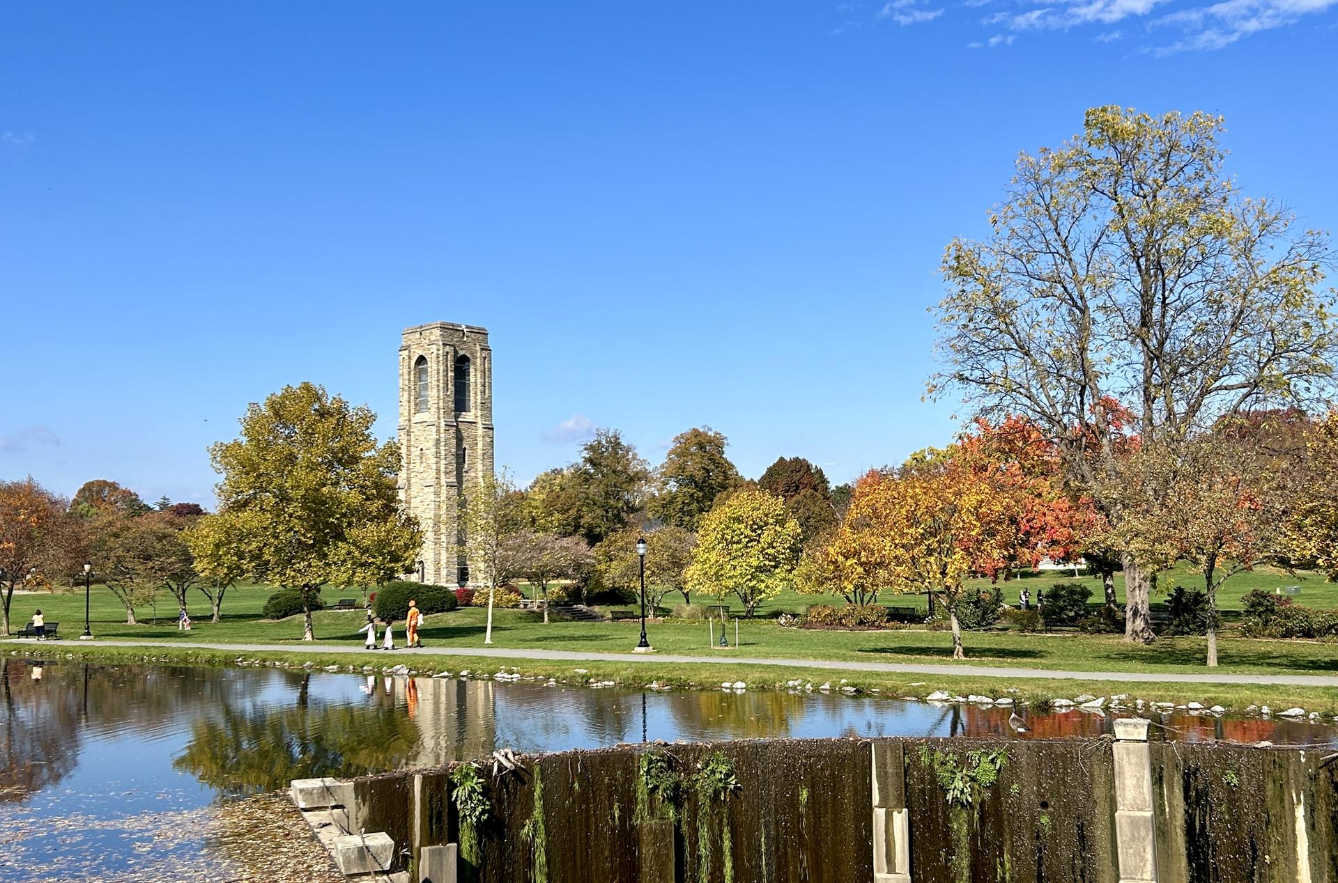 Sunny autumn day with a stone tower, colorful trees, and water reflecting the sky.