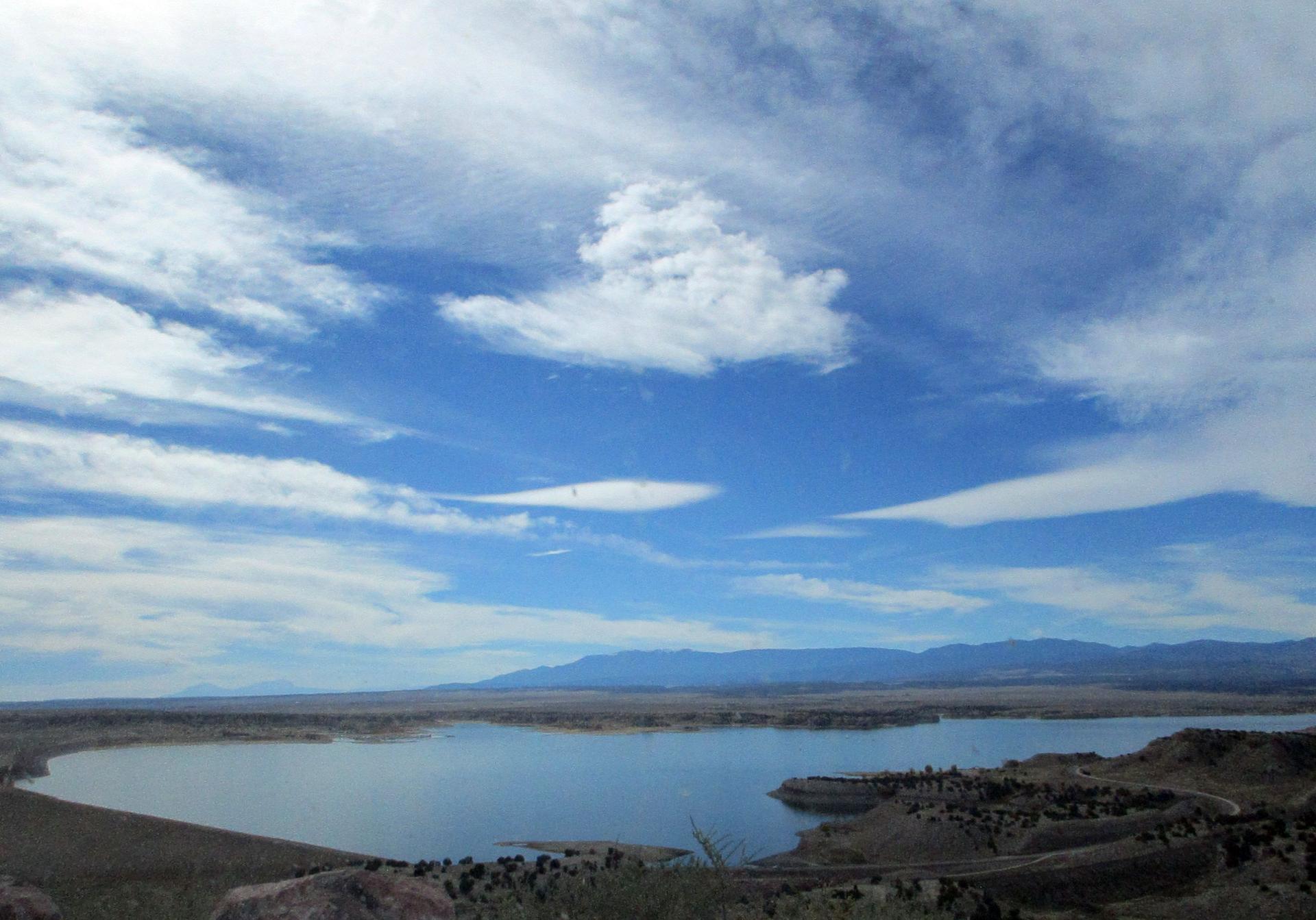 Expansive blue sky with wispy clouds over a large lake and distant mountains.