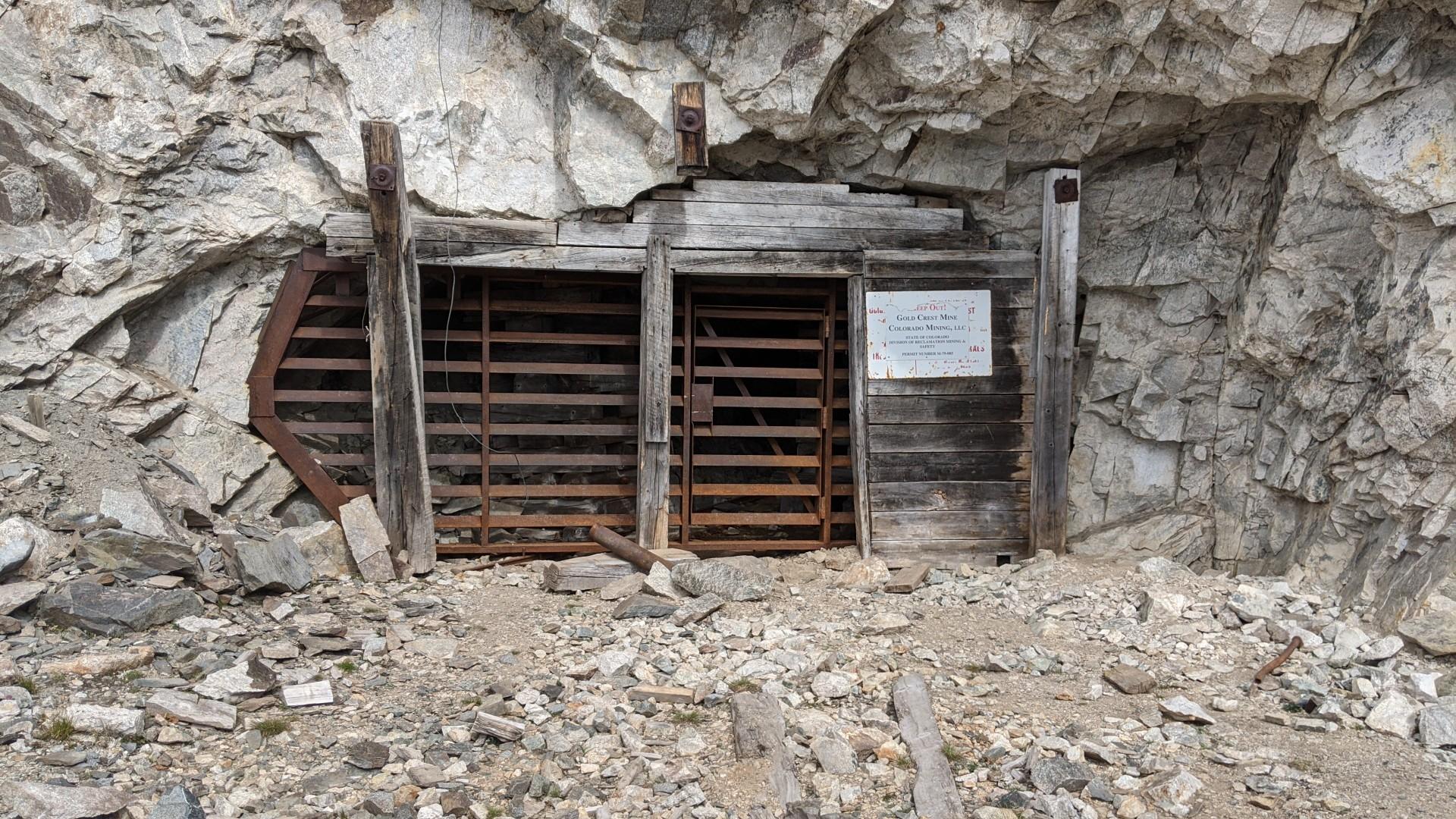 Weathered wooden mine entrance with metal grates built into a rocky cliff.