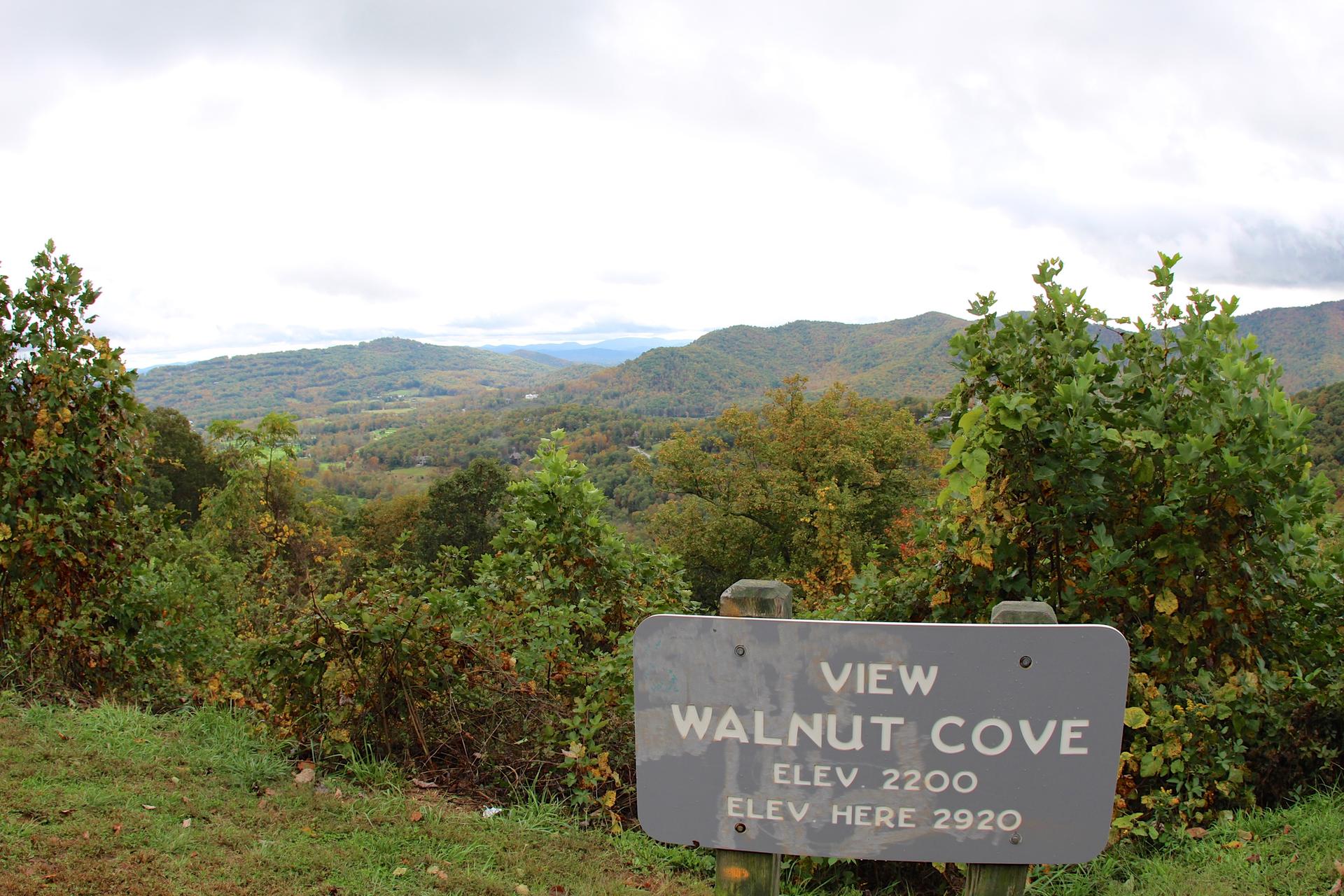 A weathered wooden sign stands before a panoramic view of distant mountains and autumn trees.