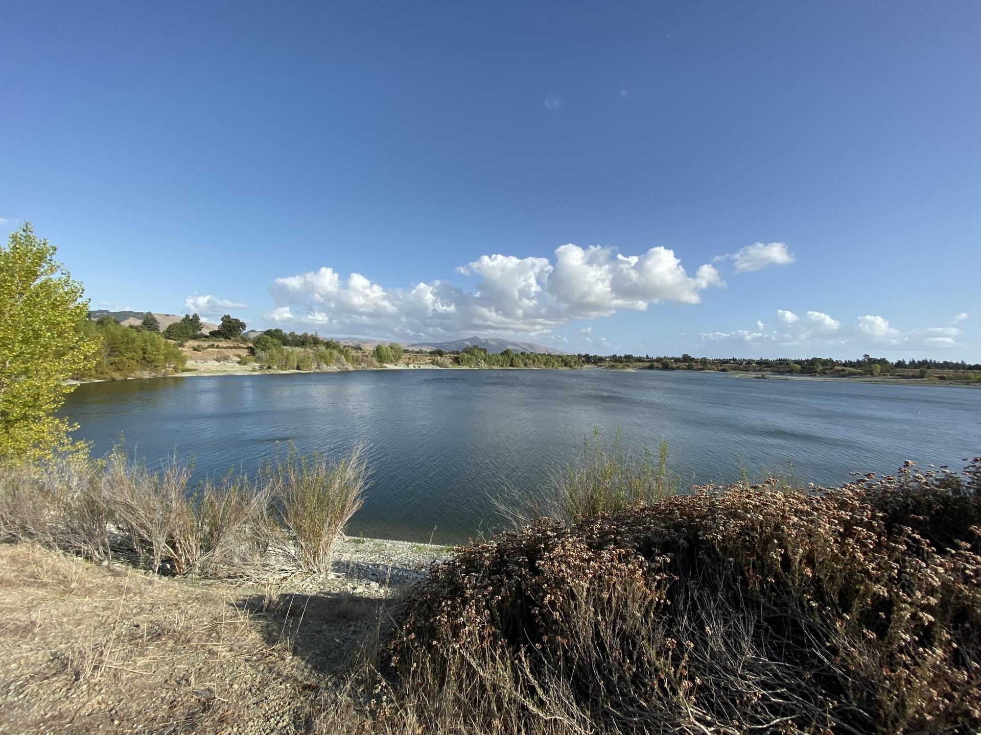 A wide lake with distant hills and a bright blue sky with white clouds.