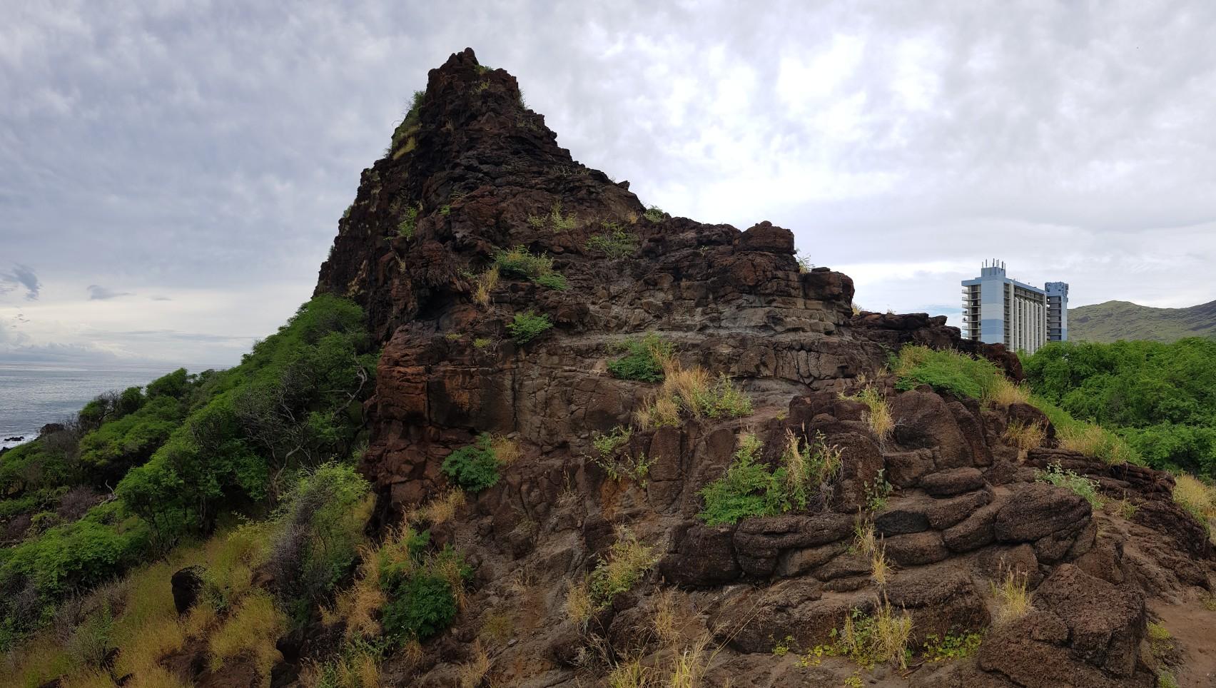A rugged, rocky peak covered in green foliage under an overcast sky.