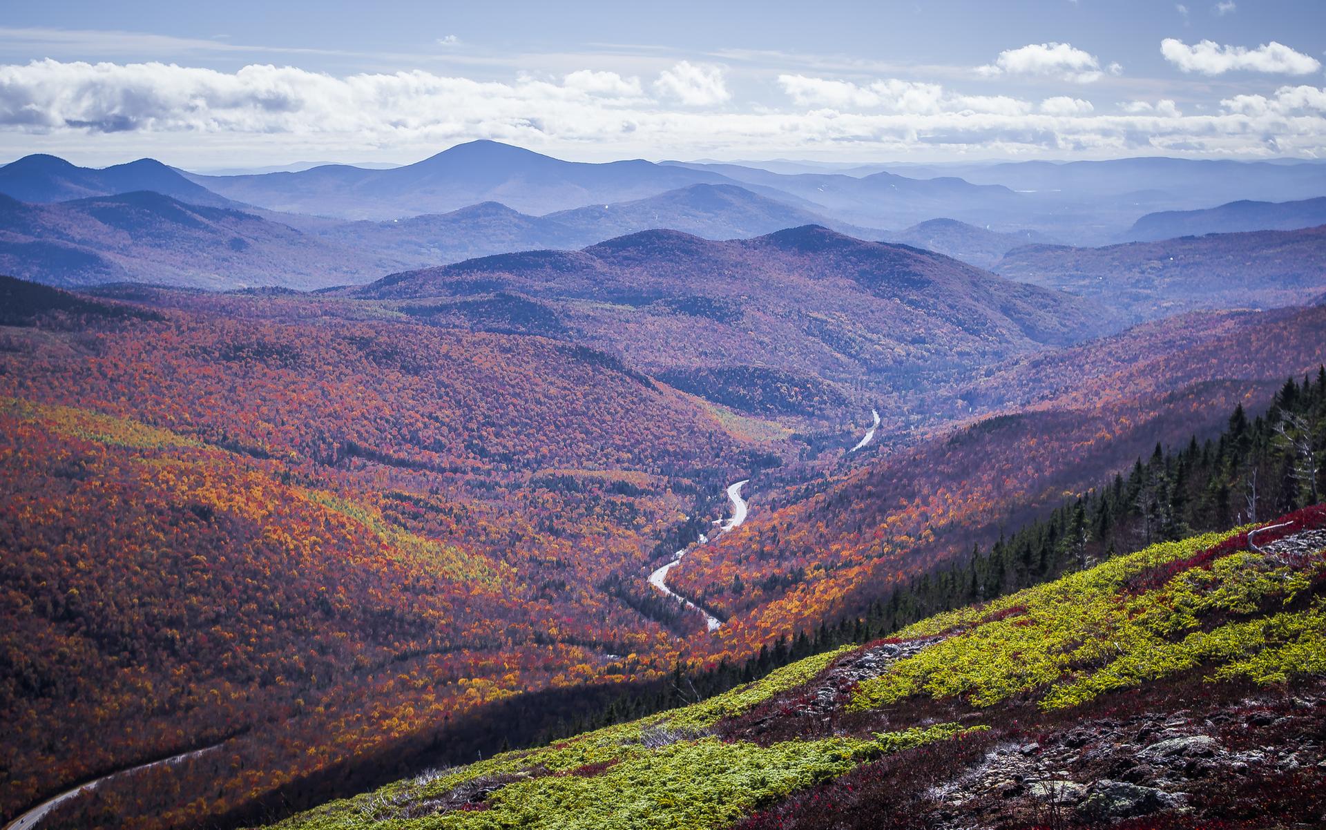 Expansive autumn valley with a winding road, distant mountains under a bright sky.