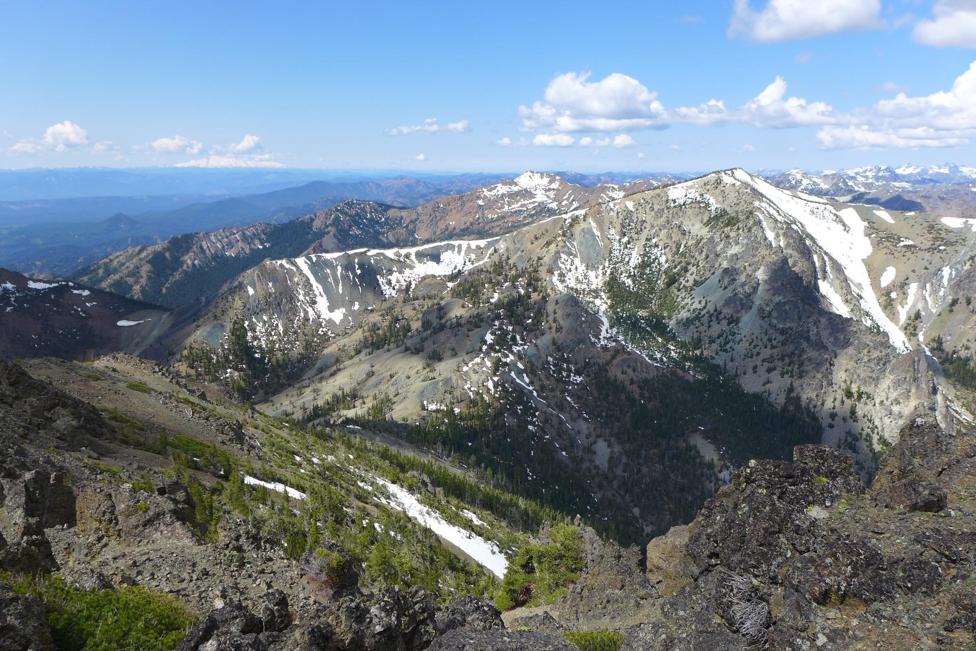 Panoramic view of rugged, snow-dusted mountains under a bright, cloudy sky.
