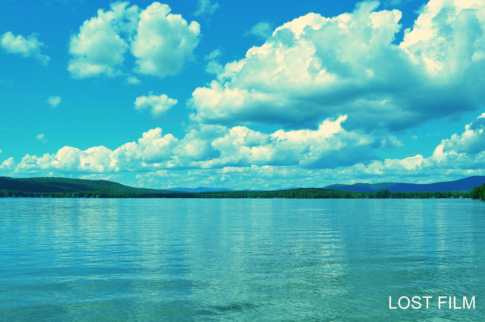 Bright blue lake with distant green hills under a cloudy sky.