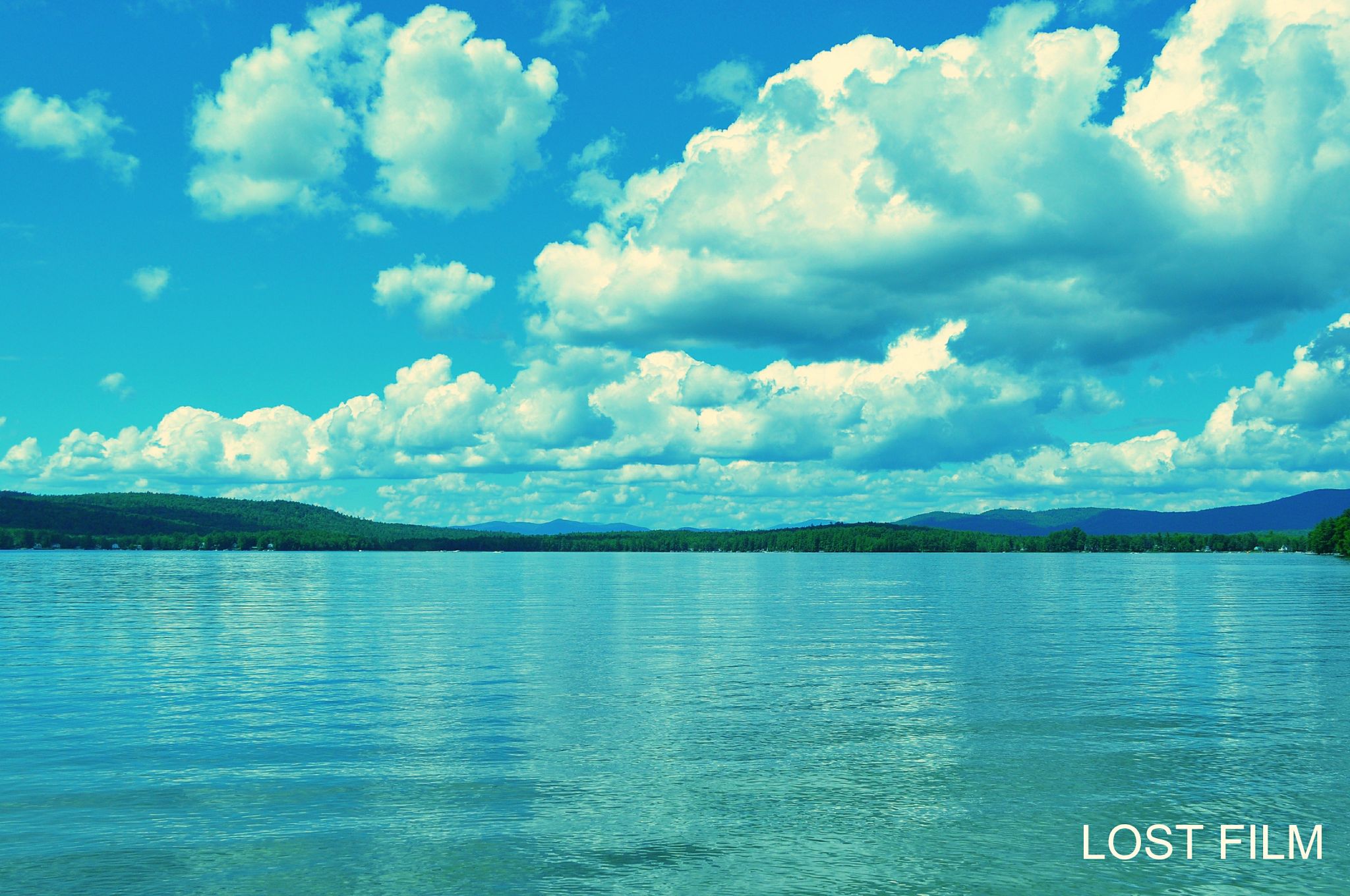 Bright blue lake with distant green hills under a cloudy sky. - Sebago Lake loop