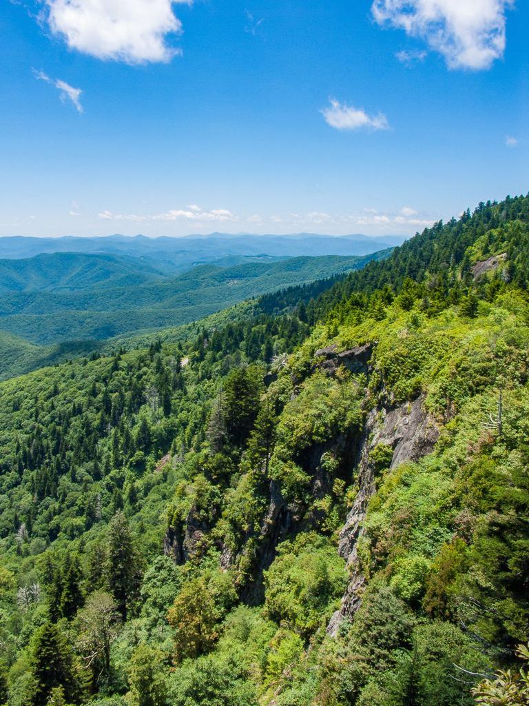 Vast green mountain range under a bright blue sky with white clouds.