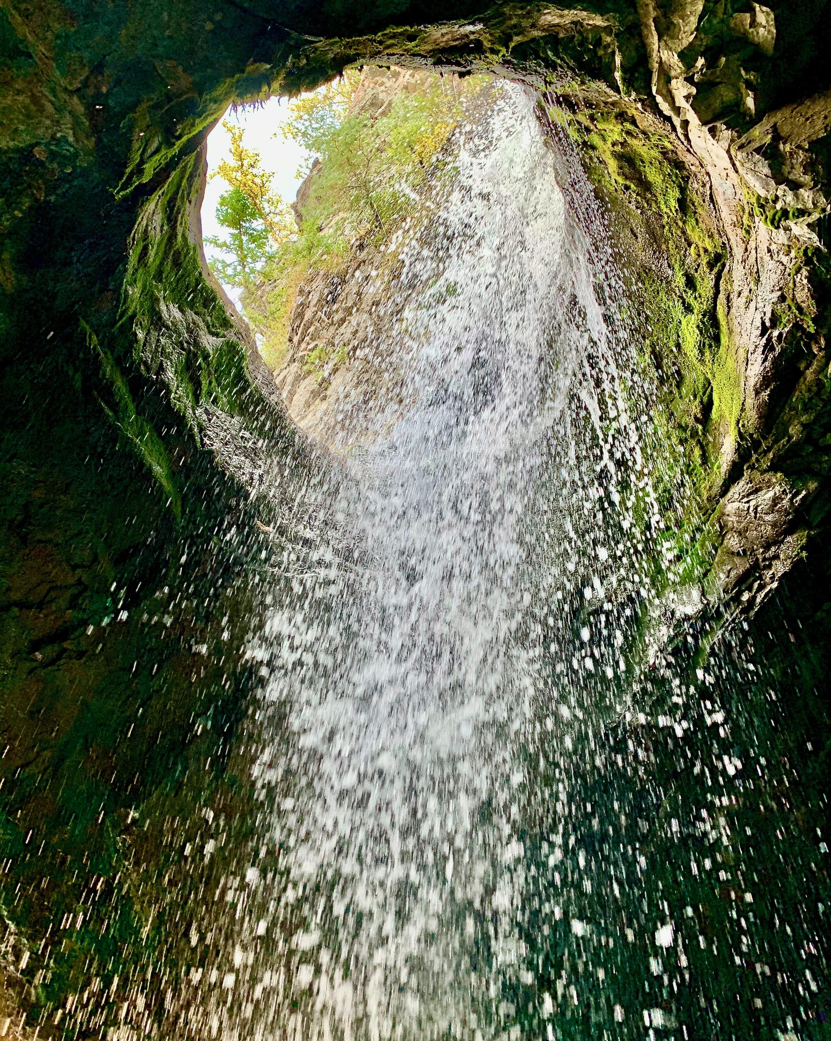 View from inside a mossy grotto with a bright waterfall cascading down.