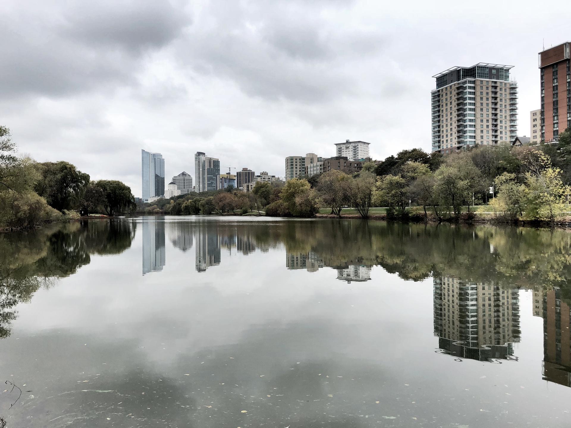 Overcast sky above a lake reflecting a city skyline and trees.