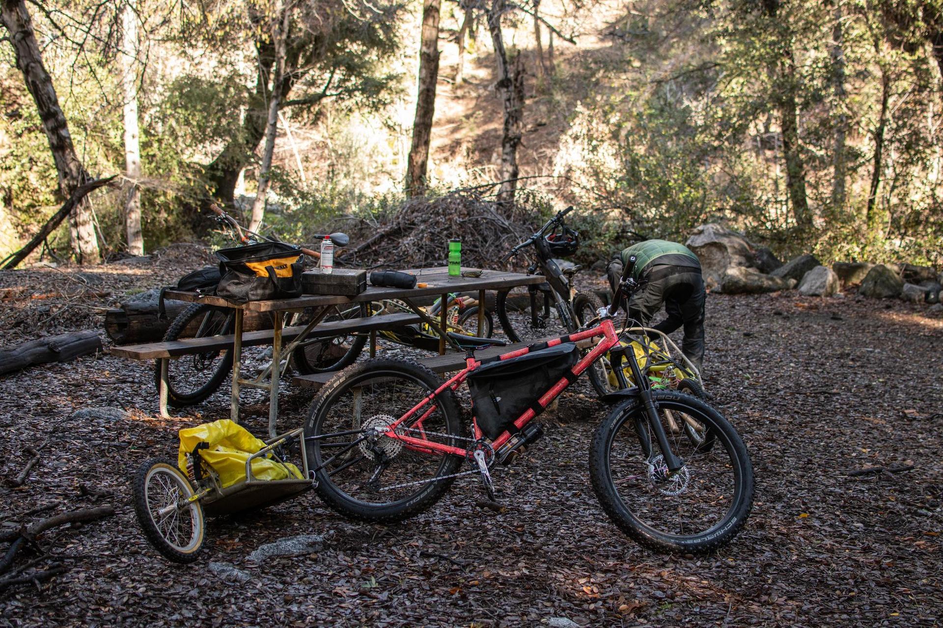 Red mountain bike with trailer parked in a forest campsite with a person.