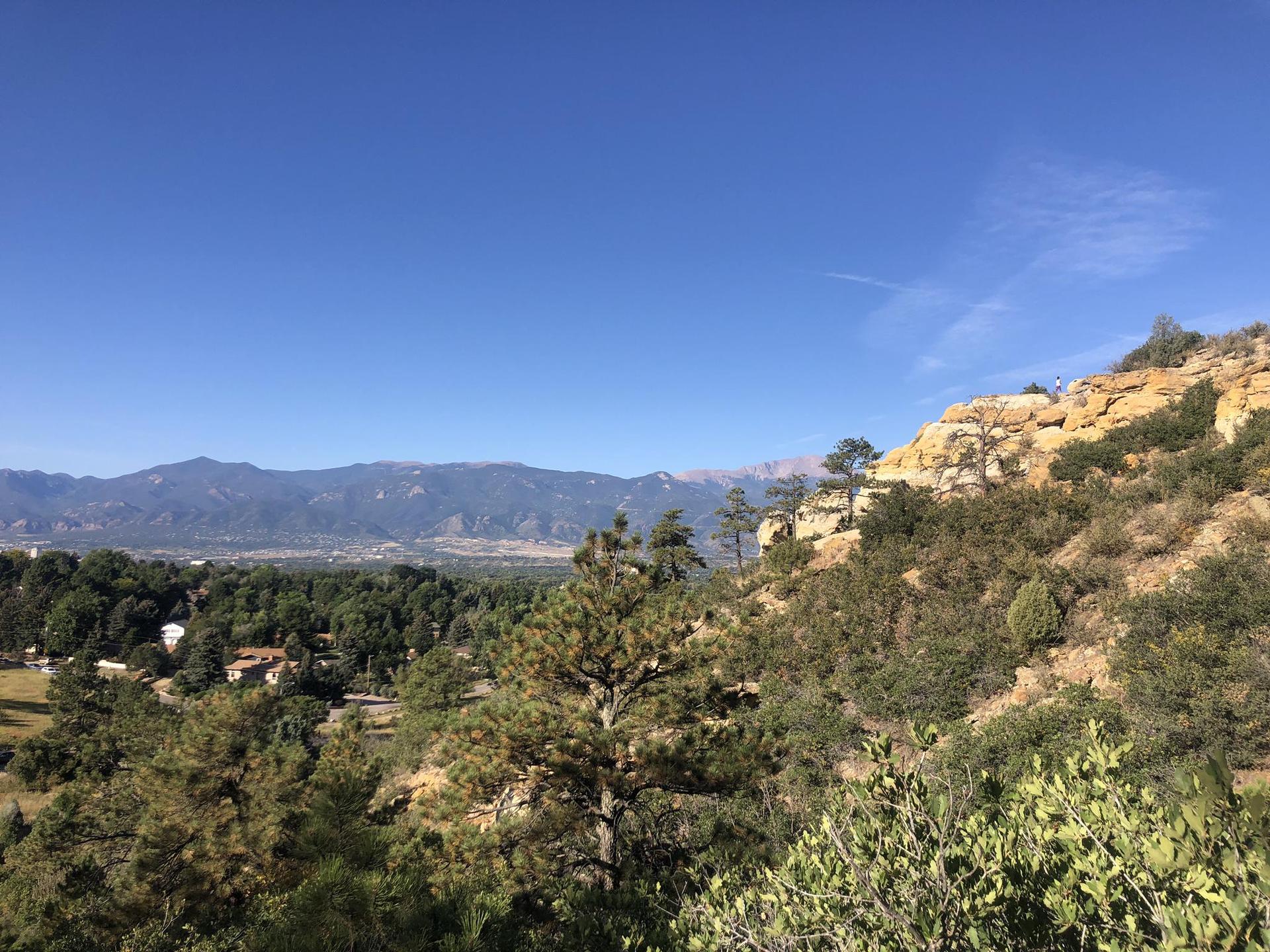 Sunny view of a green valley and distant mountains from a rocky hillside.