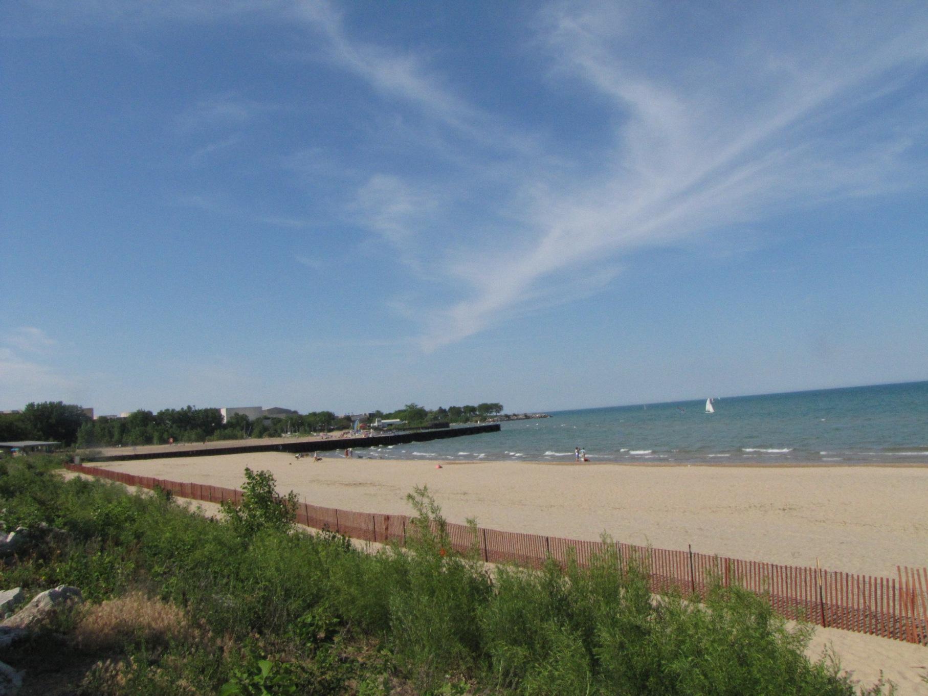 A wide sandy beach meets calm blue water under a bright sky.