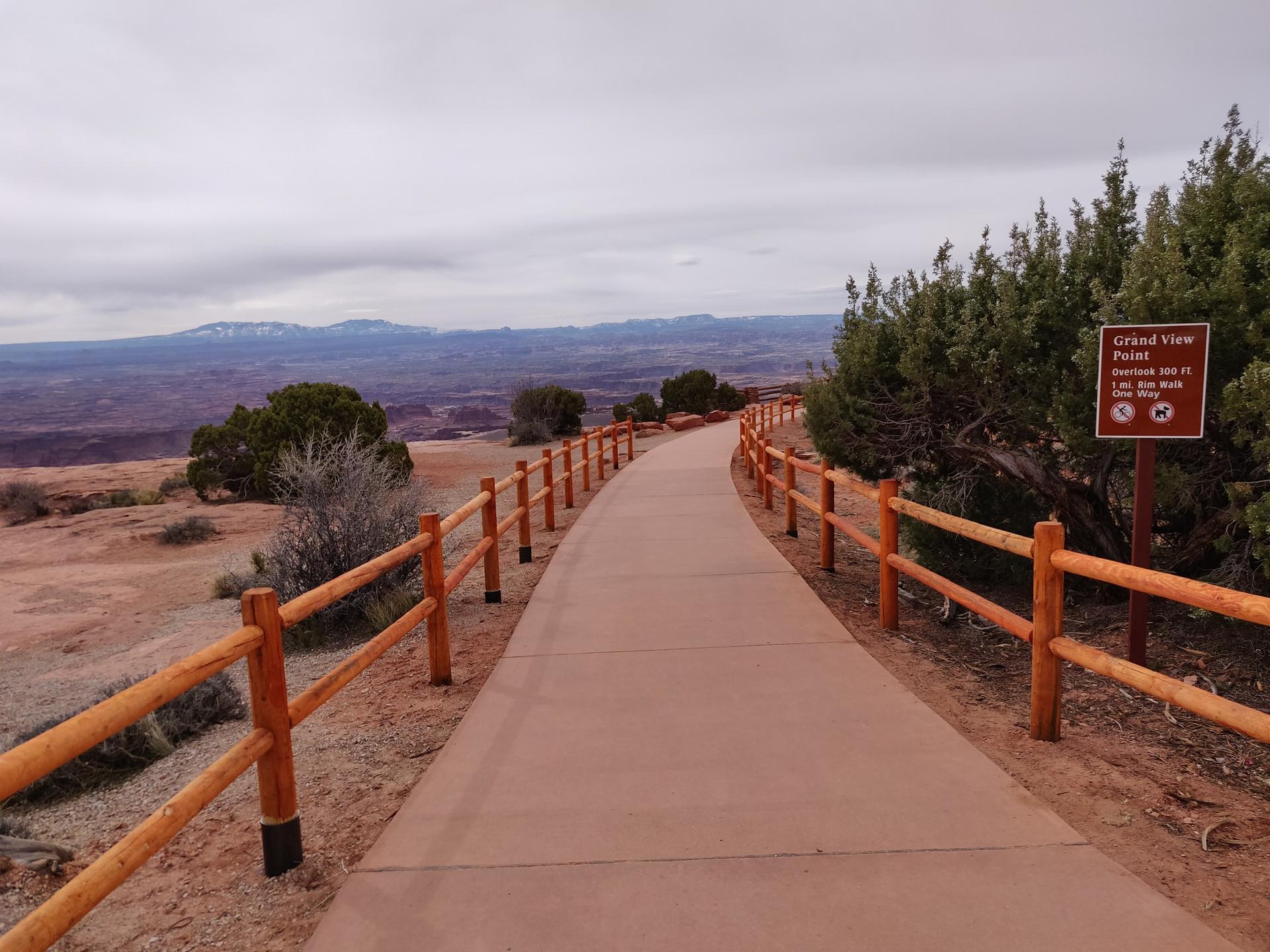 Paved path with wooden fences leading to a viewpoint under an overcast sky.