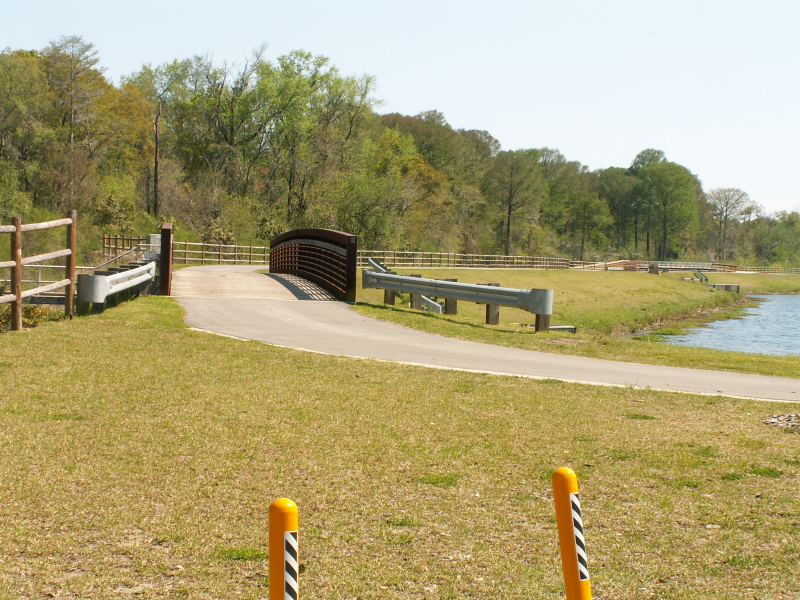 Paved path leading to a metal bridge over water on a sunny day. - Bridge at Lake Henrietta – Lake Henrietta loop from Lake Munson Dam