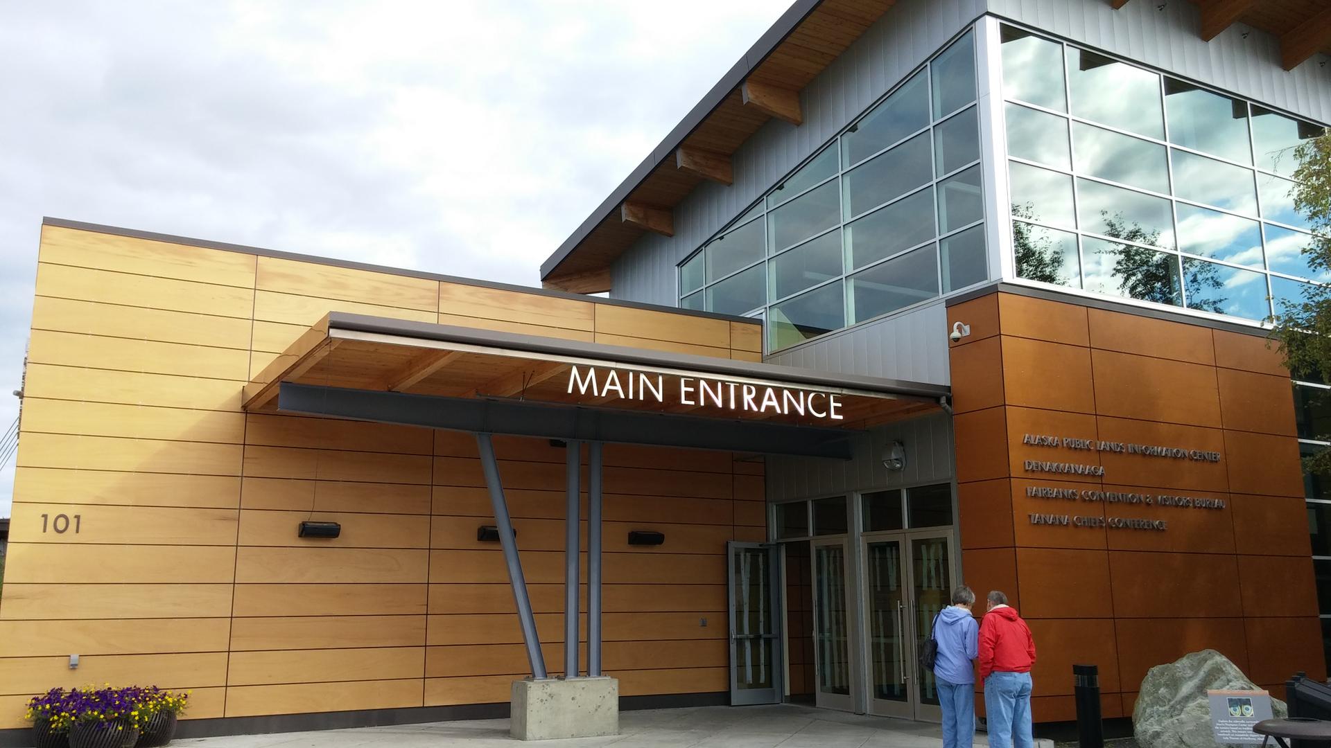 Bright daylight illuminates a modern building entrance with two people.