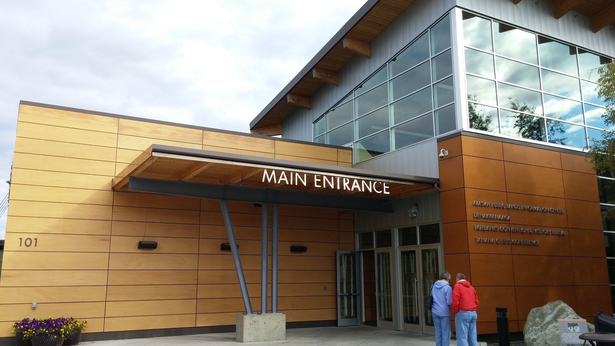 Bright daylight illuminates a modern building entrance with two people. - Urban loop run from moose antler arch