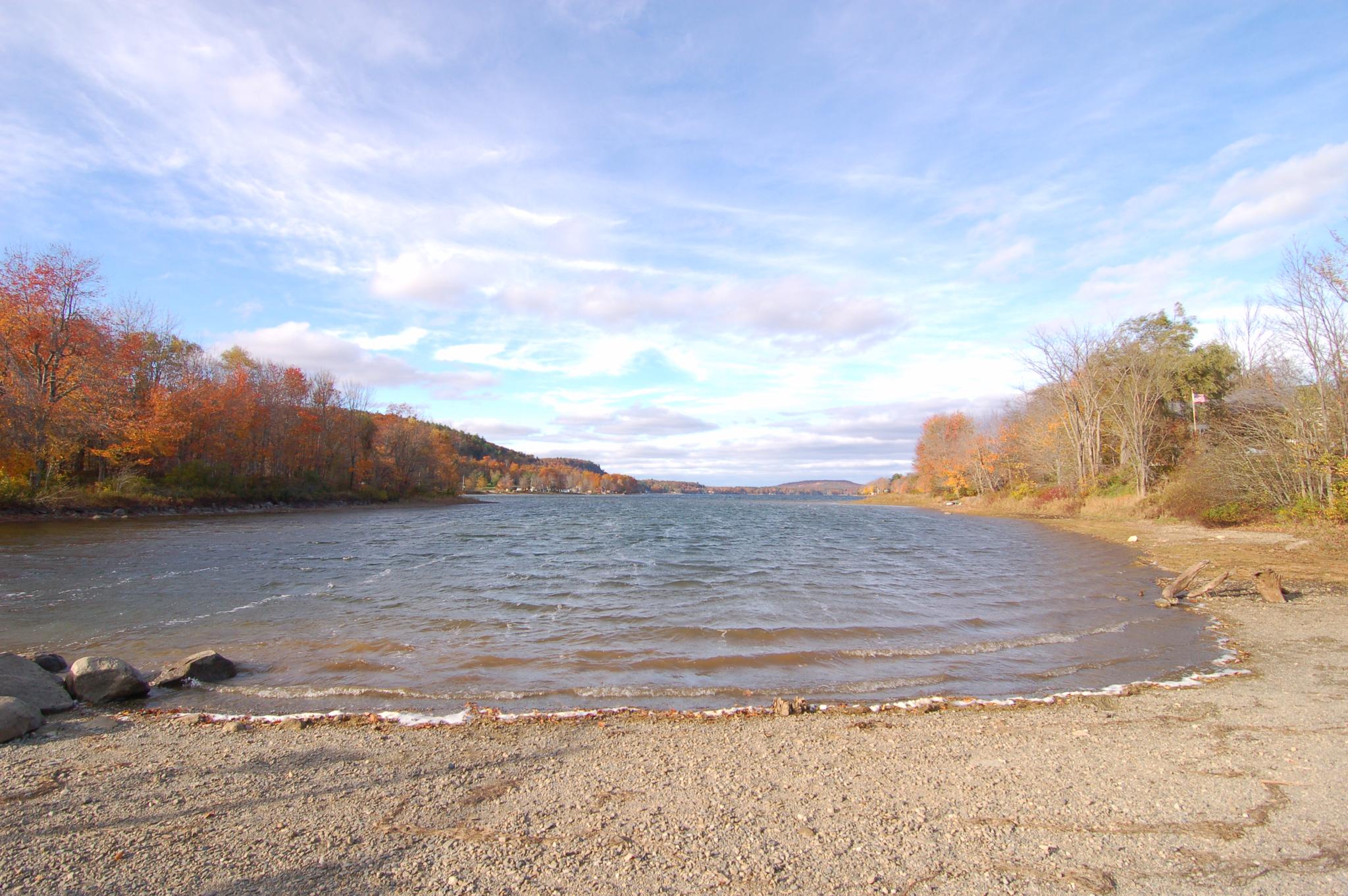 Inlet of water with a small beach and autumn trees under a cloudy sky.