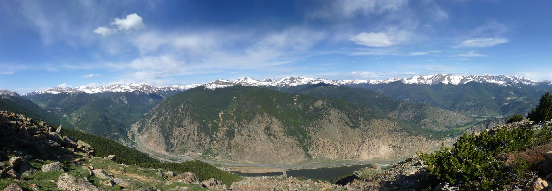 Panoramic view of vast green and rocky mountains with distant snow-capped peaks.