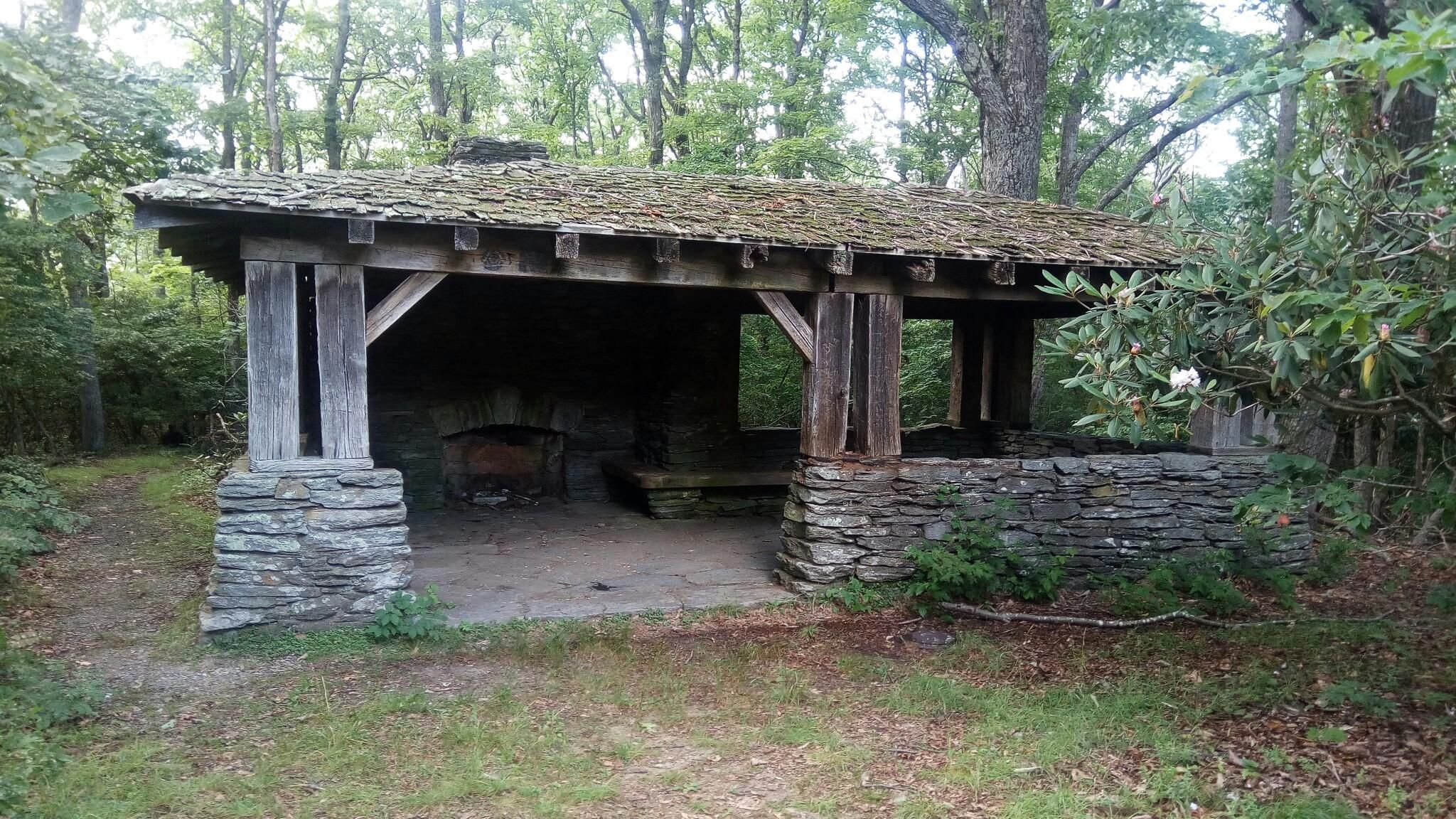 Rustic stone and wood shelter with a fireplace in a green forest. - Gully Creek Trail Loop