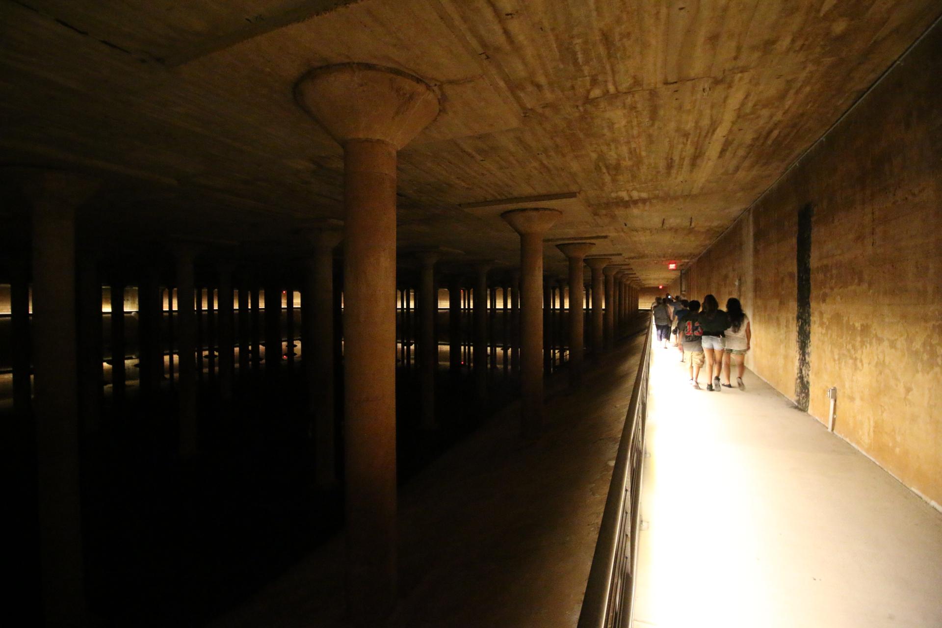 People walk along a dimly lit concrete pathway in a vast underground space.
