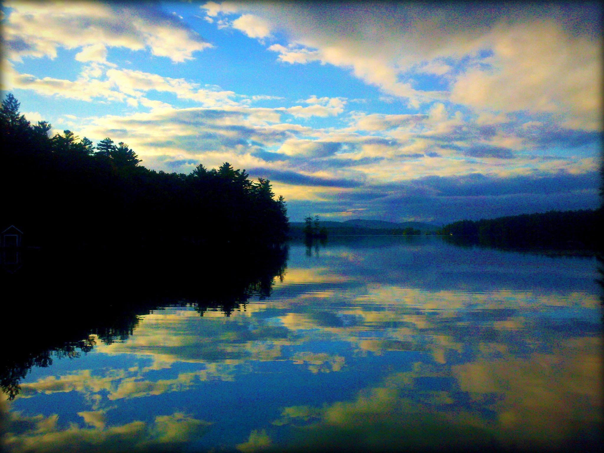 Serene lake at dusk, reflecting colorful clouds and dark forest.