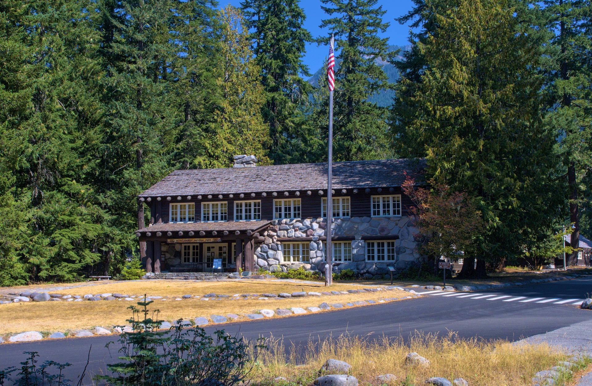 Rustic stone and wood building with a flag, surrounded by tall evergreen trees.