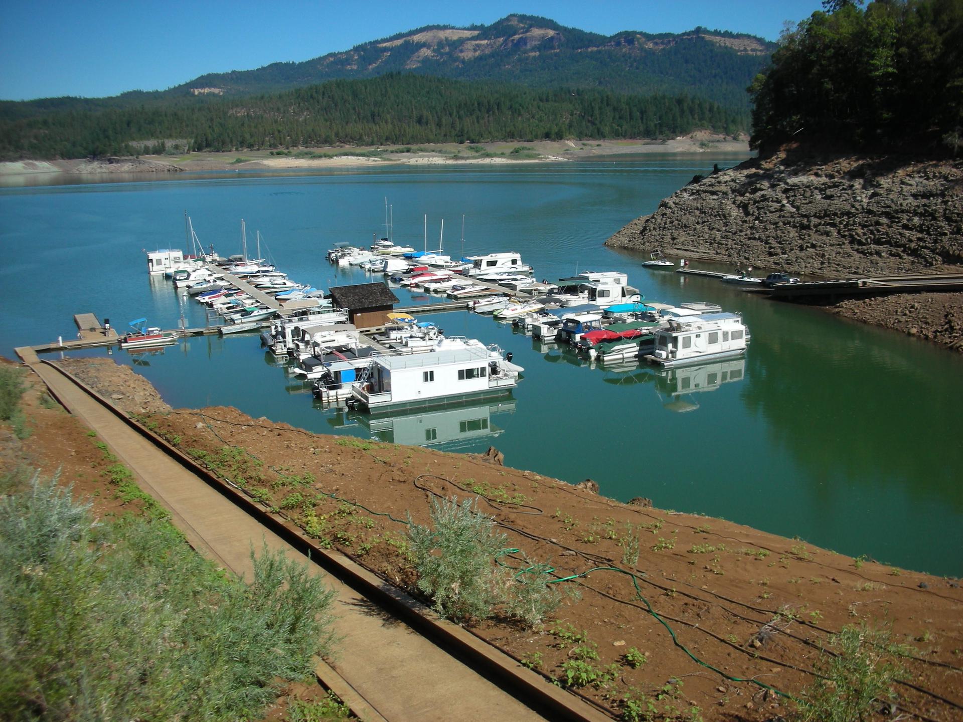 Houseboats docked at a marina on a lake, surrounded by forested hills.
