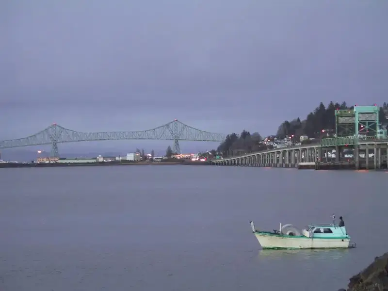 A small boat on calm water with a large bridge at dusk.
