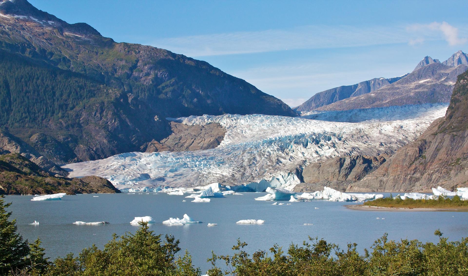 A vast blue glacier flows between rugged mountains, with icebergs floating in the lake.
