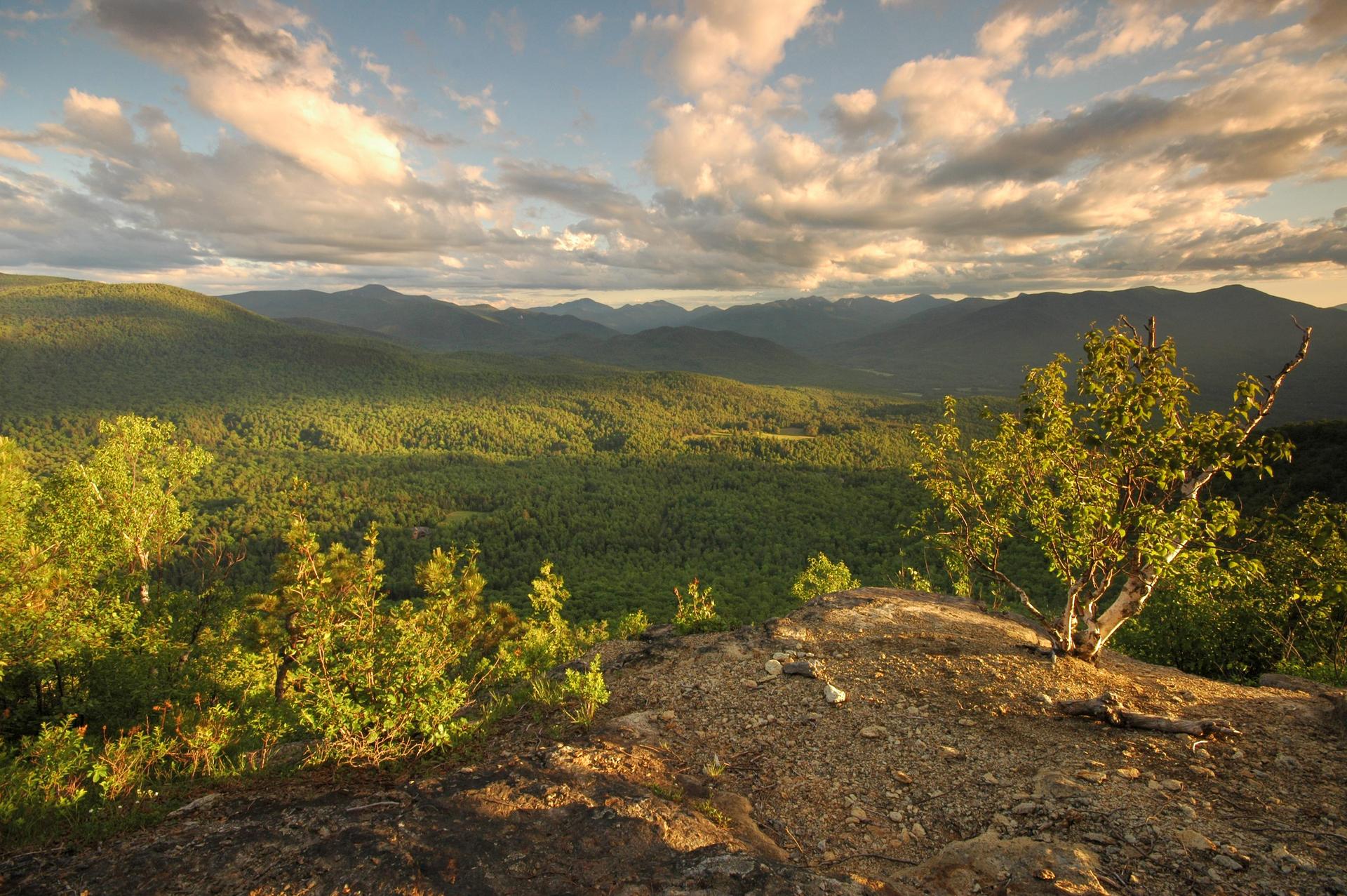 Golden light illuminates forested mountains under a dramatic cloudy sky.