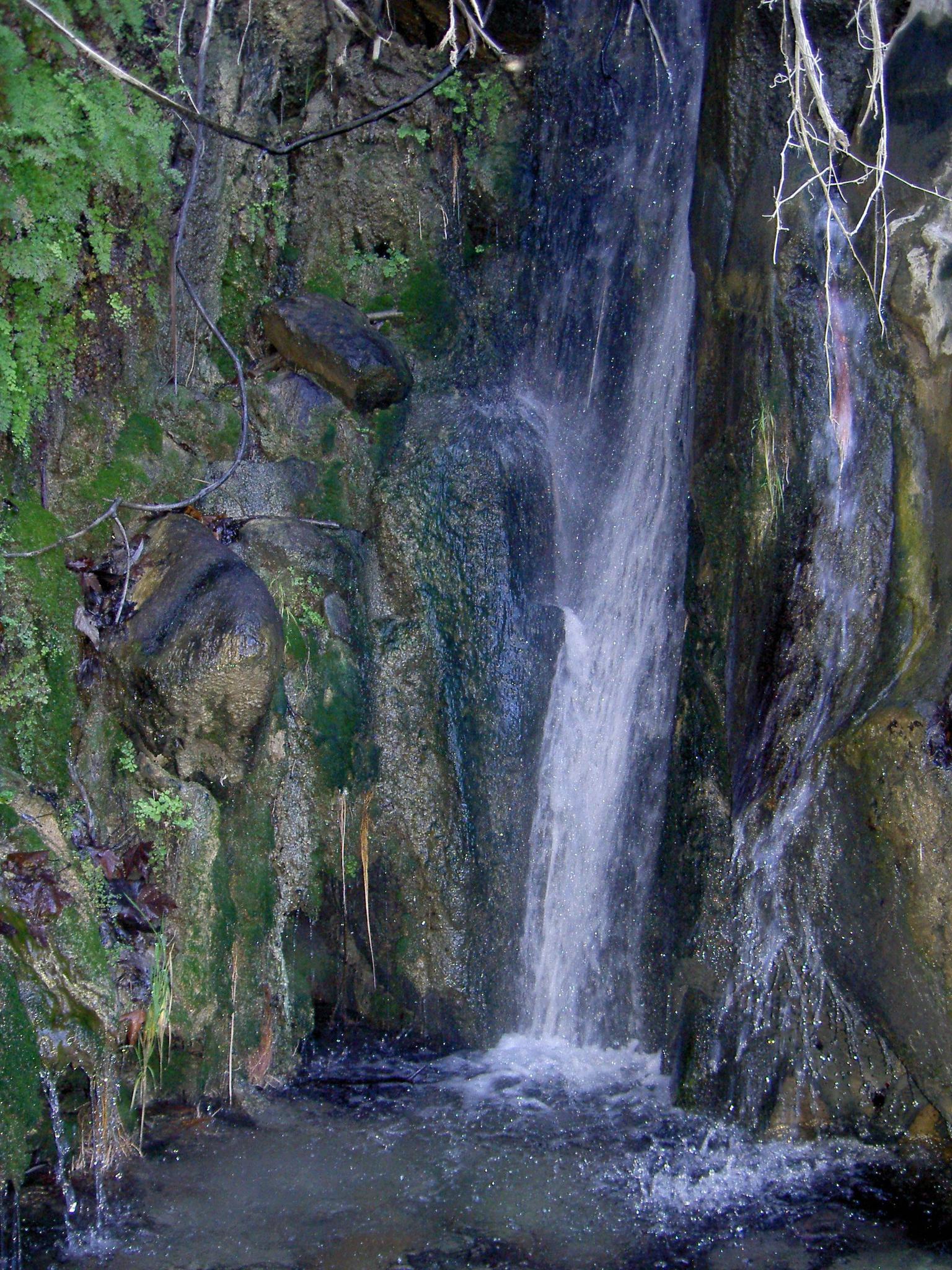 Small waterfall cascading over mossy rocks into a dark pool.