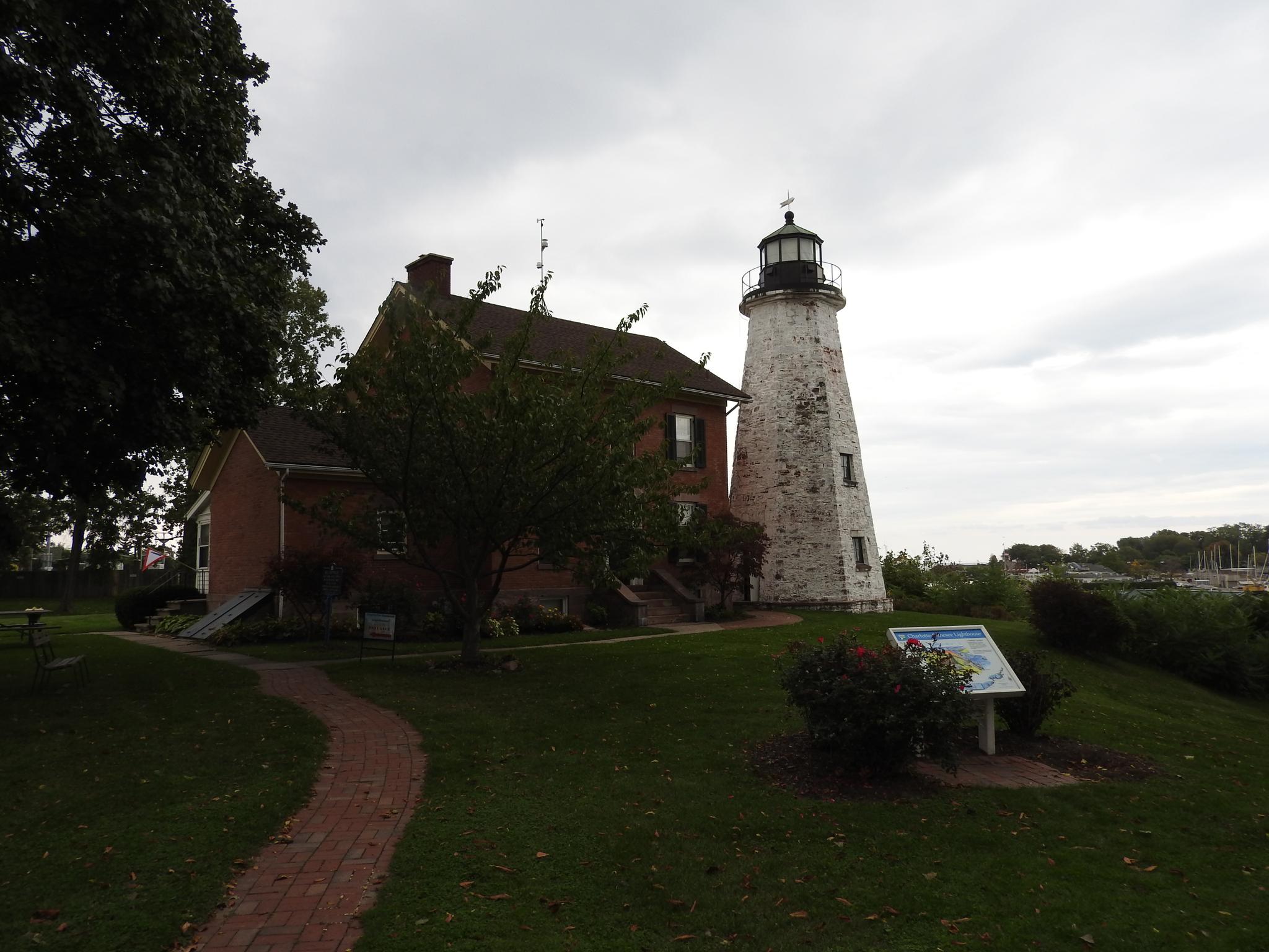 A brick house and white lighthouse stand on a grassy hill, overcast sky.