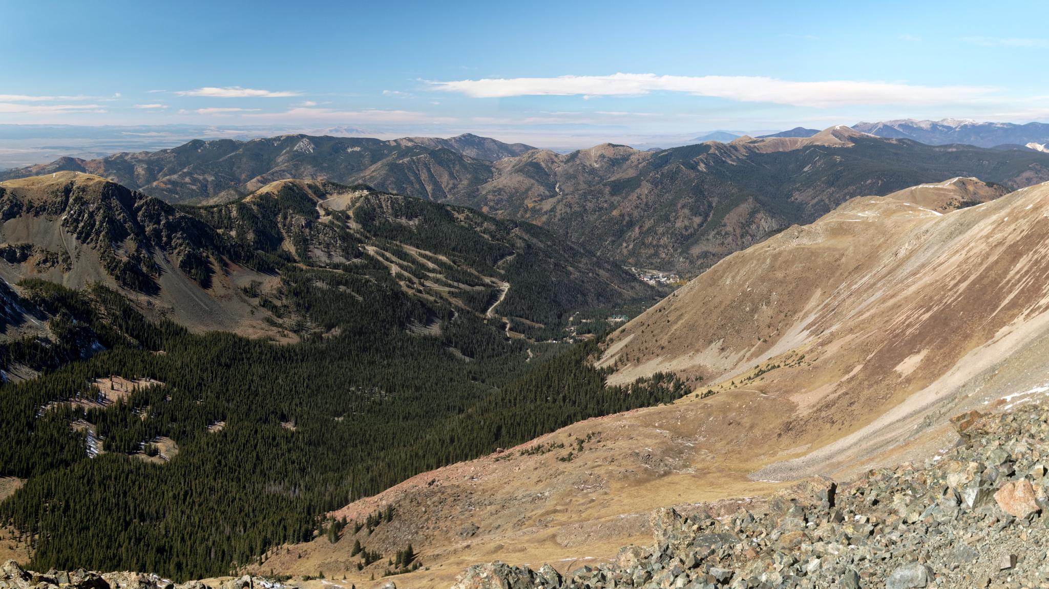 Vast mountain range with a deep valley, dense forest, and clear skies.