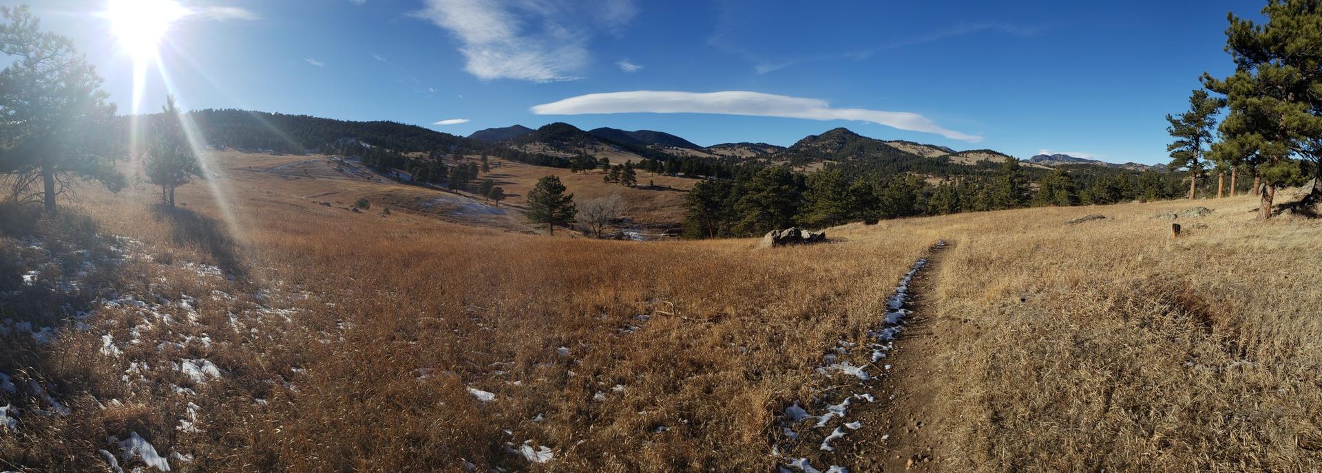Panoramic view of a vast golden field with distant mountains under a bright sun.