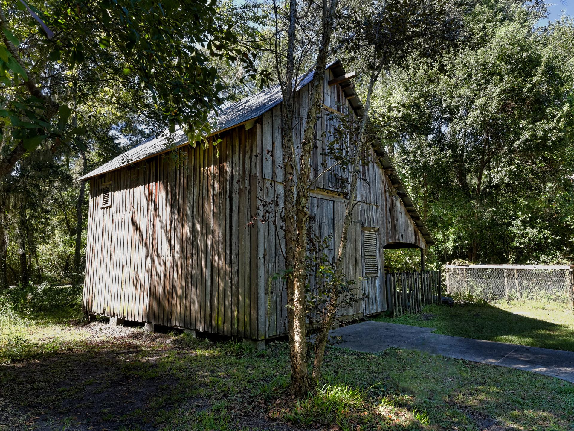 Weathered wooden barn surrounded by lush green trees under bright sun.