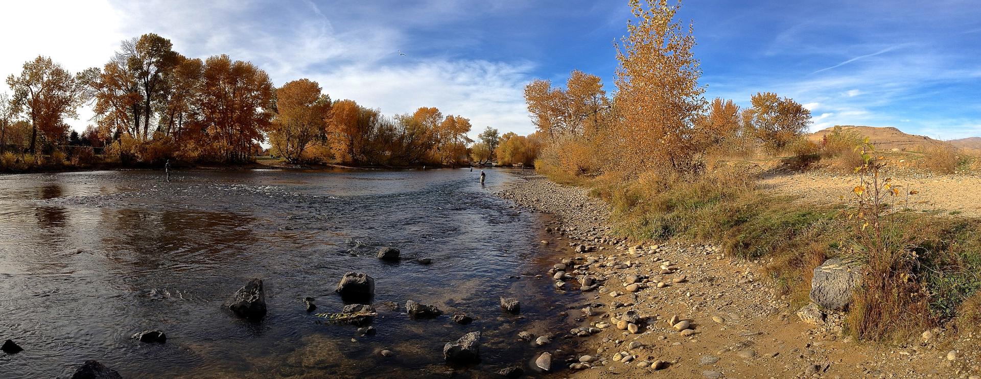 Panoramic view of a river with autumn trees and a person fishing.