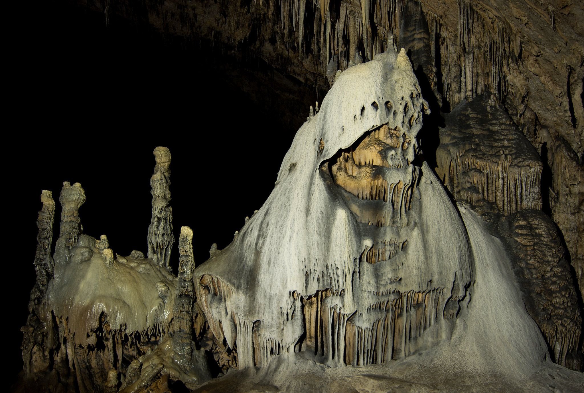 Intricate stalactites and stalagmites illuminated in a dark cave interior. - Slaughter Canyon Cave Trail
