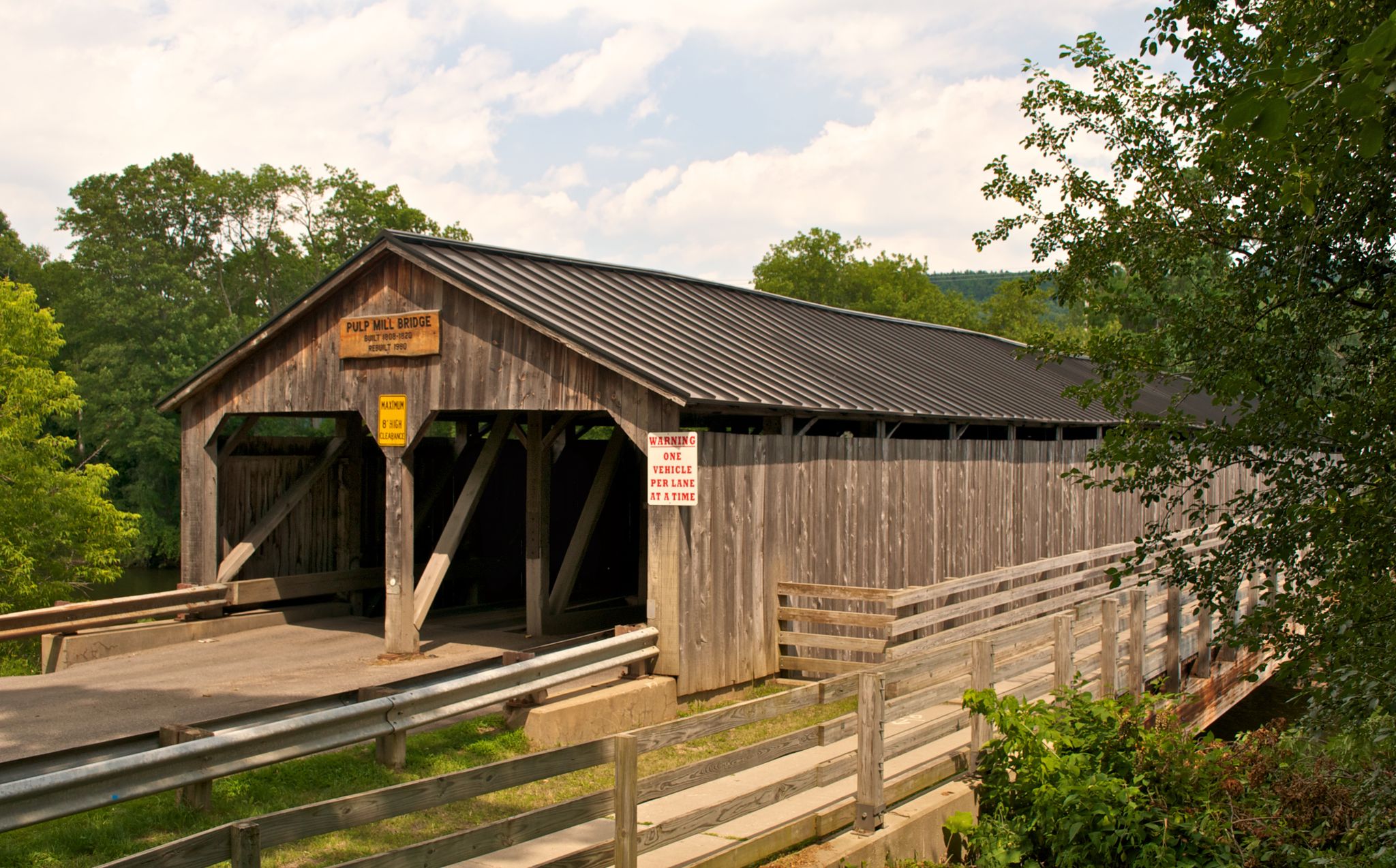 Rustic wooden covered bridge surrounded by green trees under a bright sky. - Pulp Mill Covered Bridge loop from Middlebury