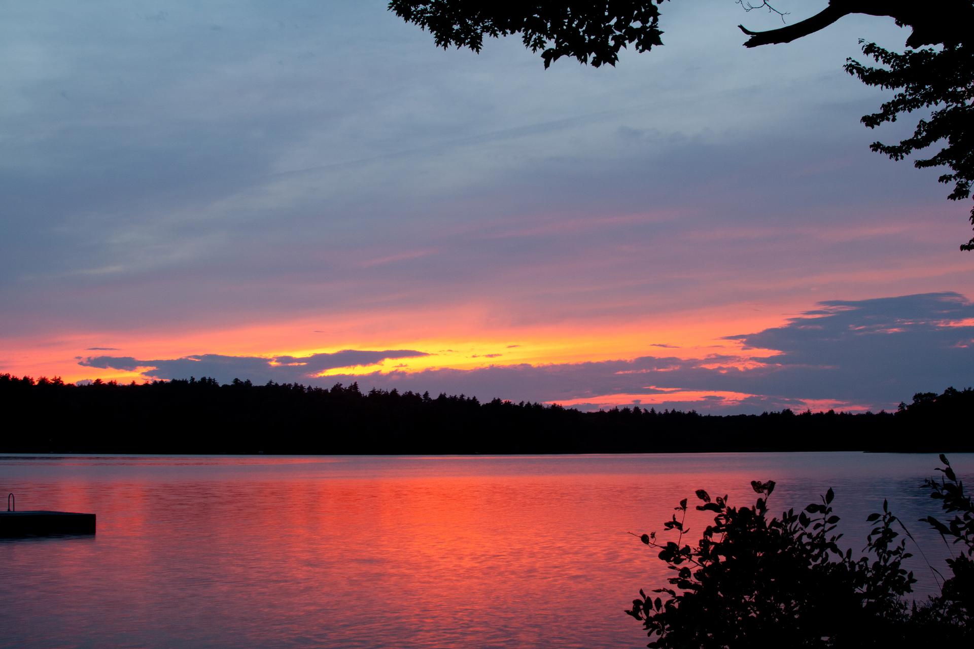 Vibrant sunset over a lake with a forest silhouette and a small dock.