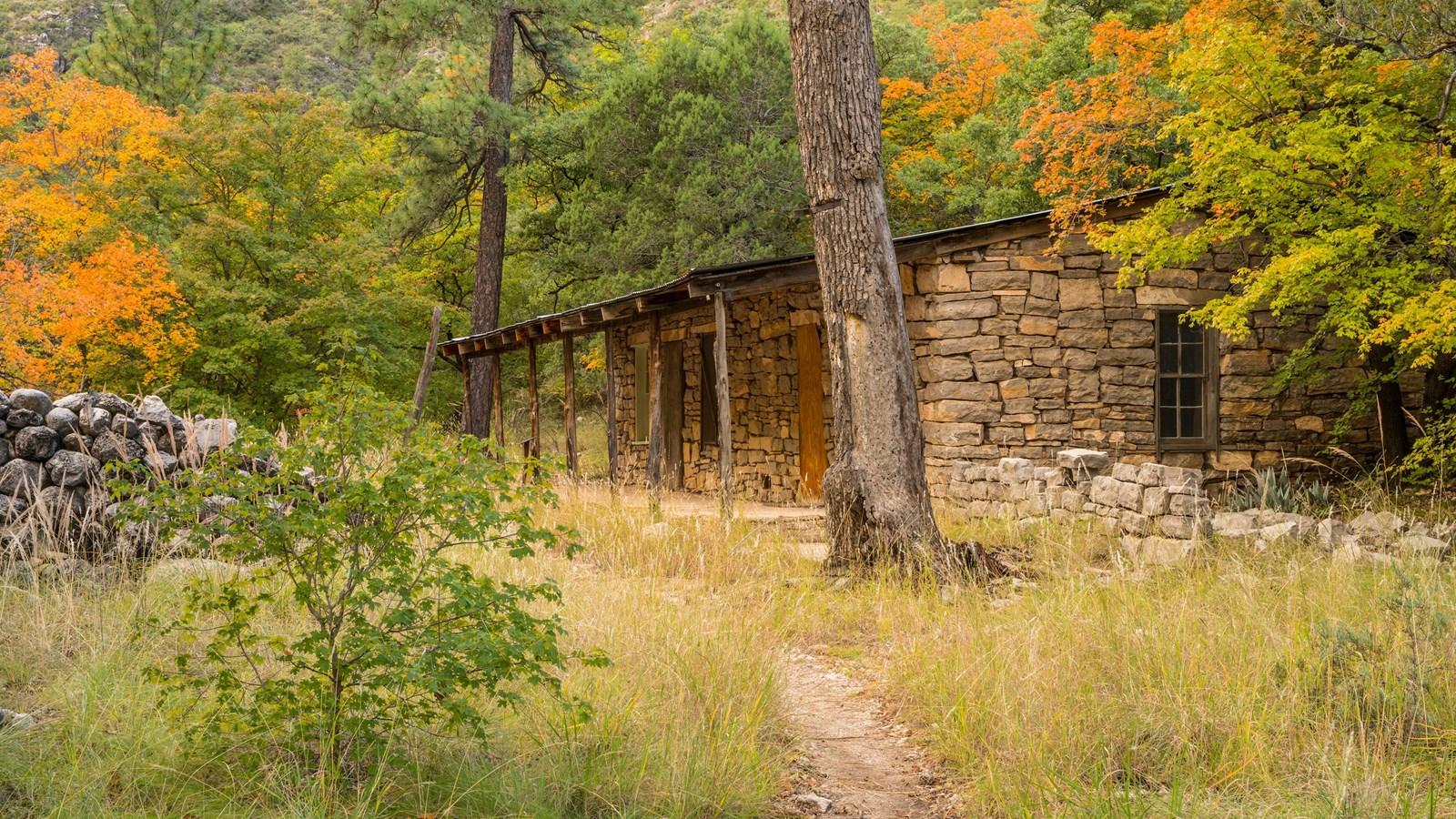 An old stone building with a porch sits among colorful autumn trees.